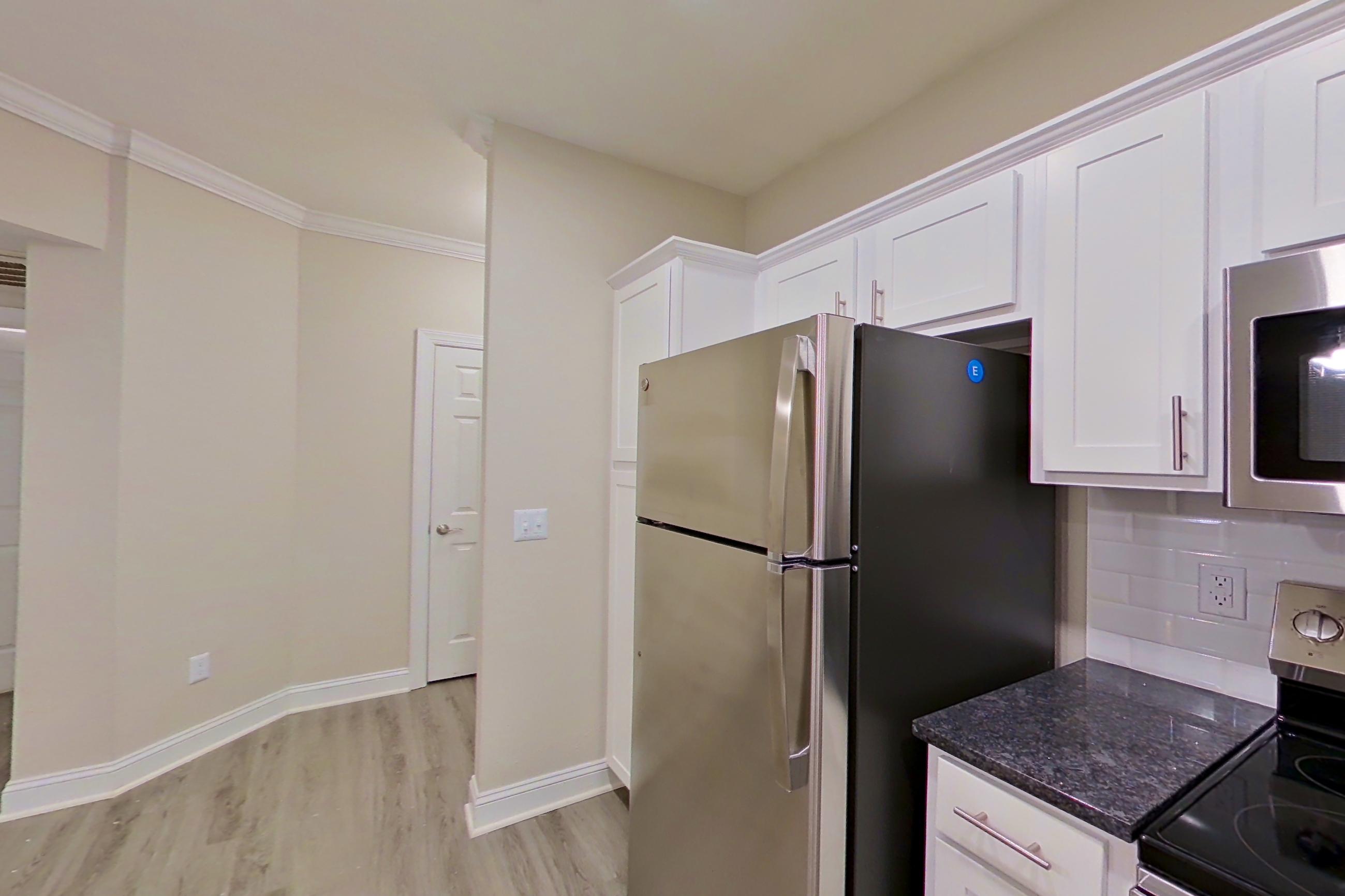 Kitchen with dark stone countertops, dishwasher, electric range, light wood-finish flooring, microwave, oven/range, refrigerator, and stainless steel appliances, Apartment 3213 at Marq Perimeter