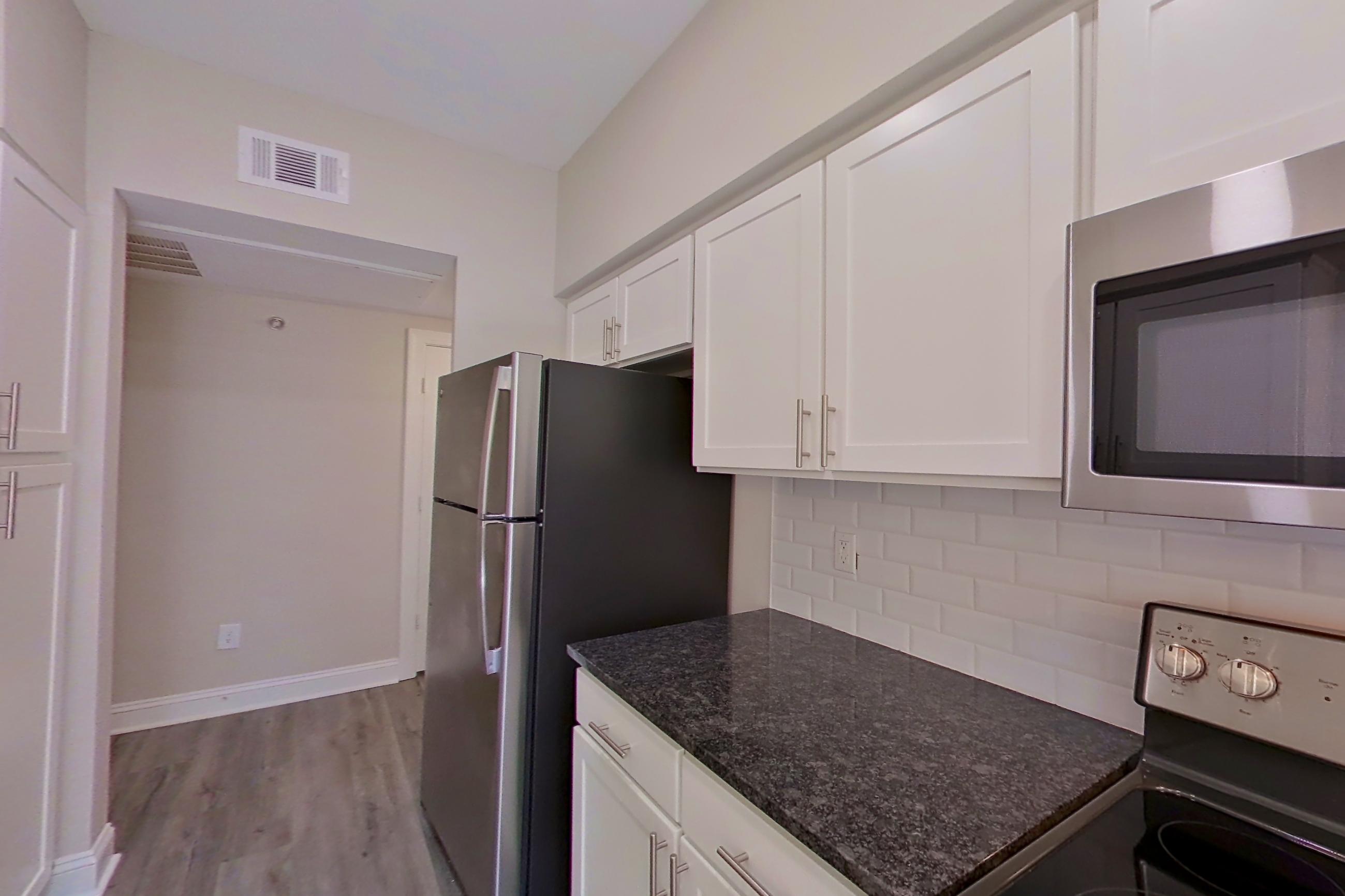 Kitchen with dark stone countertops, dishwasher, electric range, light countertops, light wood-finish flooring, oven/range, refrigerator, and stainless steel appliances, Apartment 3308 at Marq Perimeter
