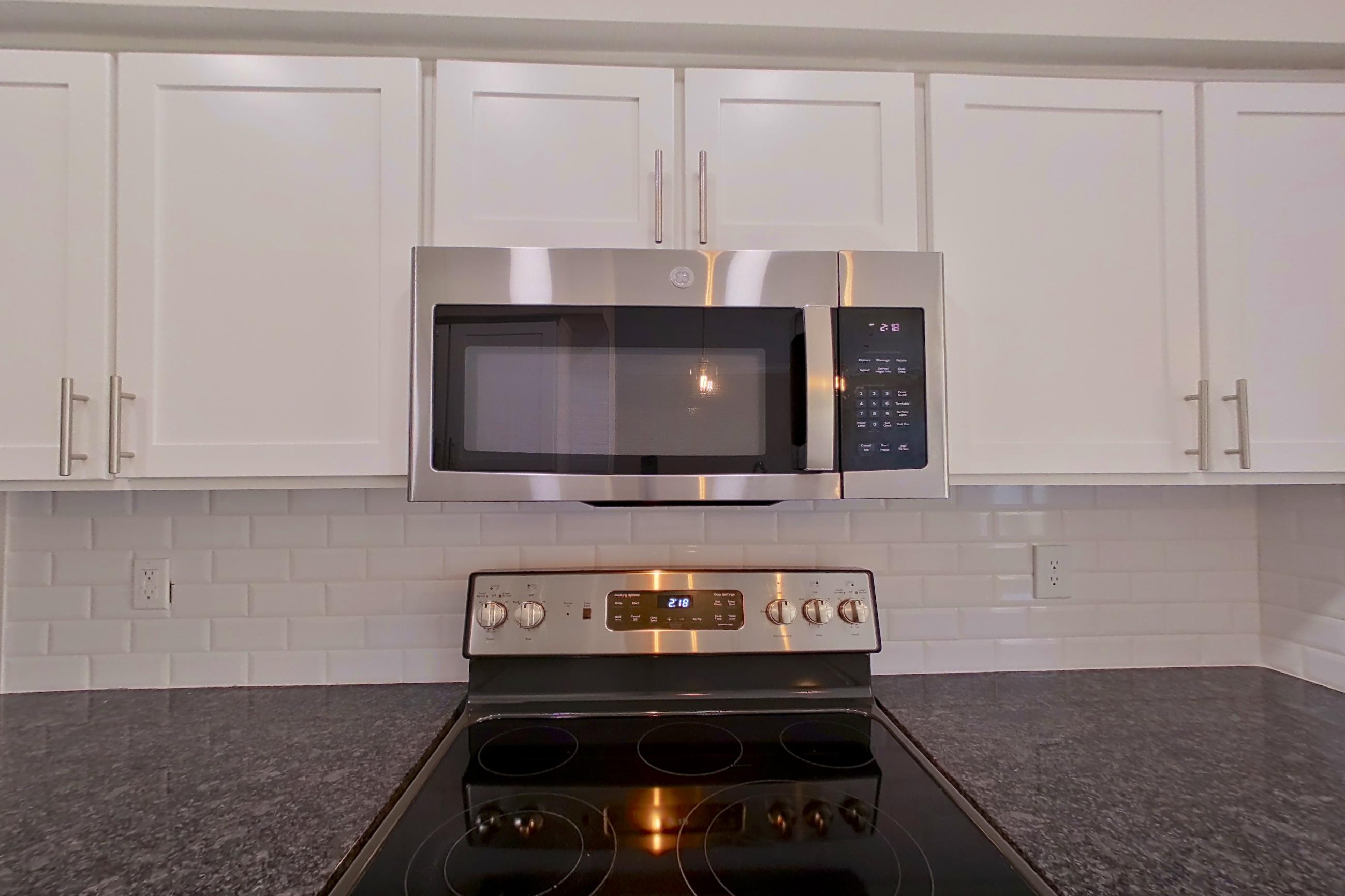 Kitchen with dark stone countertops, dishwasher, electric range, light countertops, light wood-finish flooring, oven/range, refrigerator, and stainless steel appliances, Apartment 3308 at Marq Perimeter