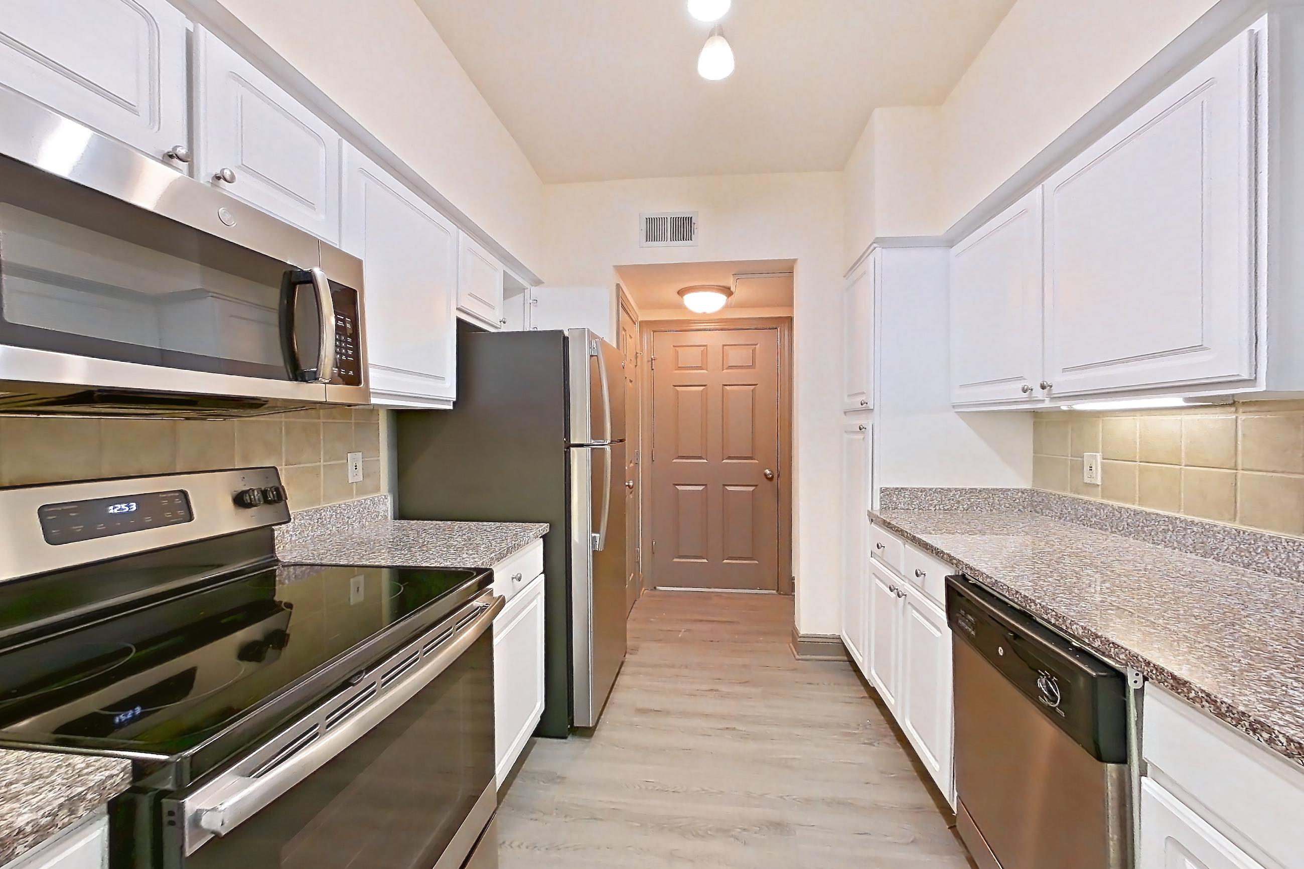 Kitchen with dark stone countertops, dishwasher, electric range, light carpet, light countertops, light stone countertops, light wood-finish flooring, microwave, oven/range, refrigerator, and stainless steel appliances, Apartment 3311 at Marq Perimeter