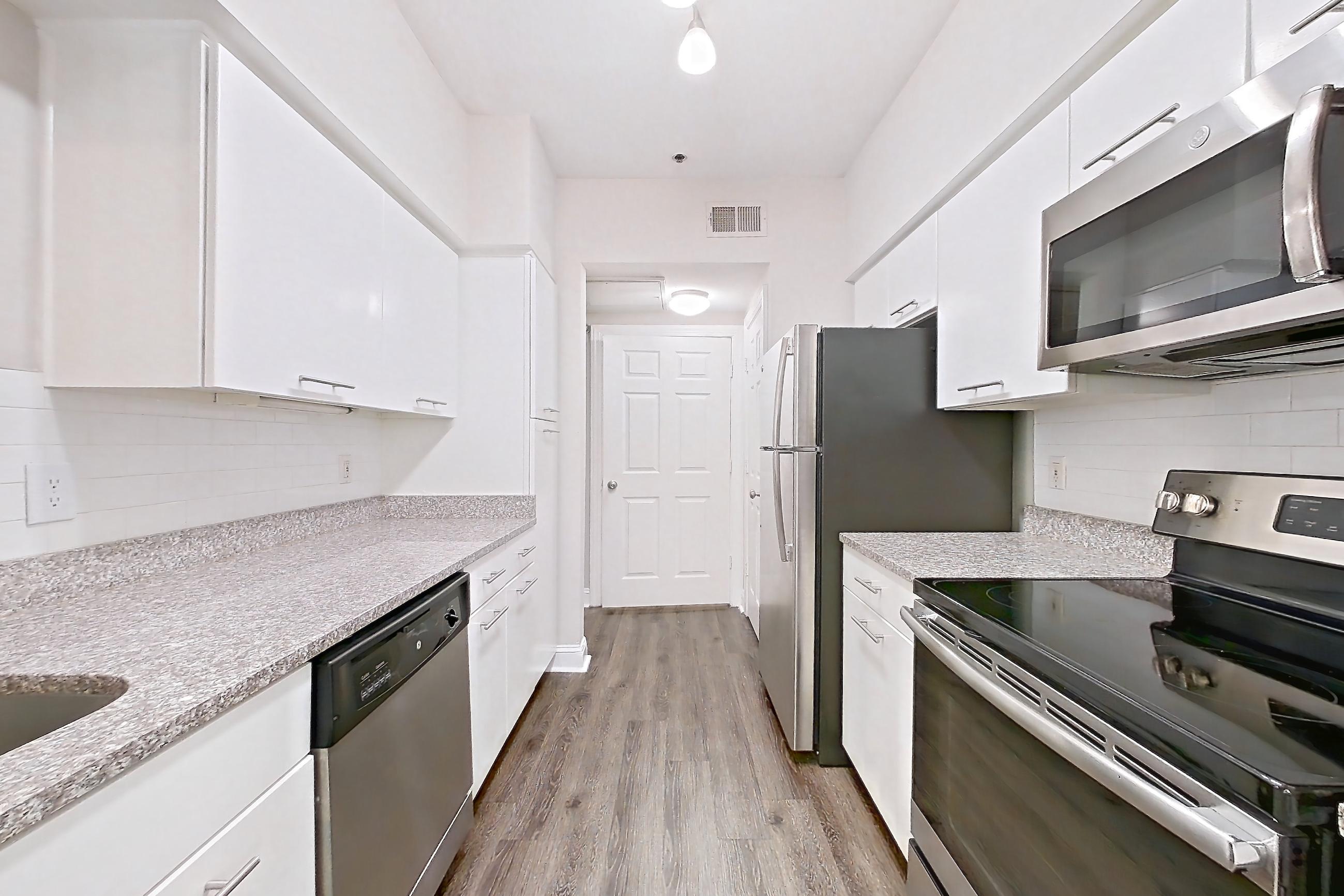 Kitchen with dark carpet, dark wood-finish flooring, dishwasher, electric range, light countertops, light stone countertops, microwave, oven/range, refrigerator, and stainless steel appliances, Apartment 3401 at Marq Perimeter