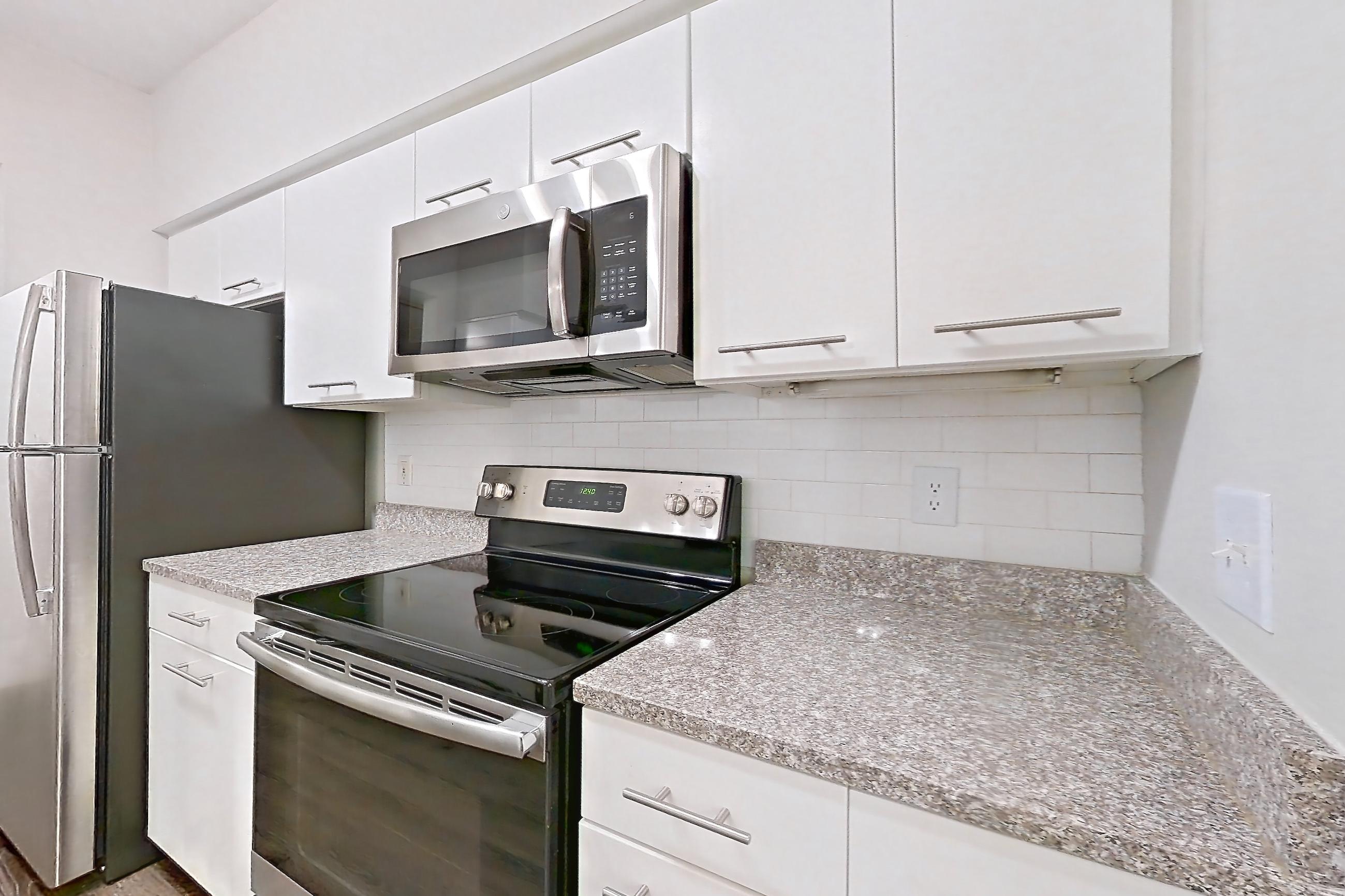 Kitchen with dark carpet, dark wood-finish flooring, dishwasher, electric range, light countertops, light stone countertops, microwave, oven/range, refrigerator, and stainless steel appliances, Apartment 3401 at Marq Perimeter