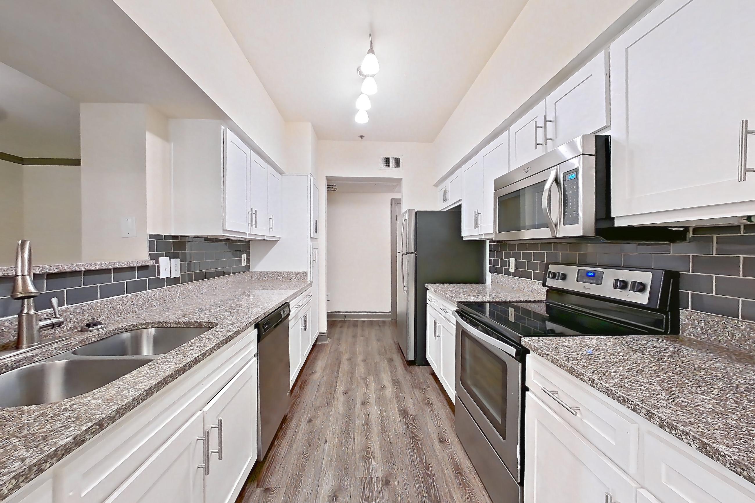Kitchen with dark wood-finish flooring, dishwasher, electric range, light stone countertops, microwave, oven/range, and stainless steel appliances, Apartment 3407 at Marq Perimeter