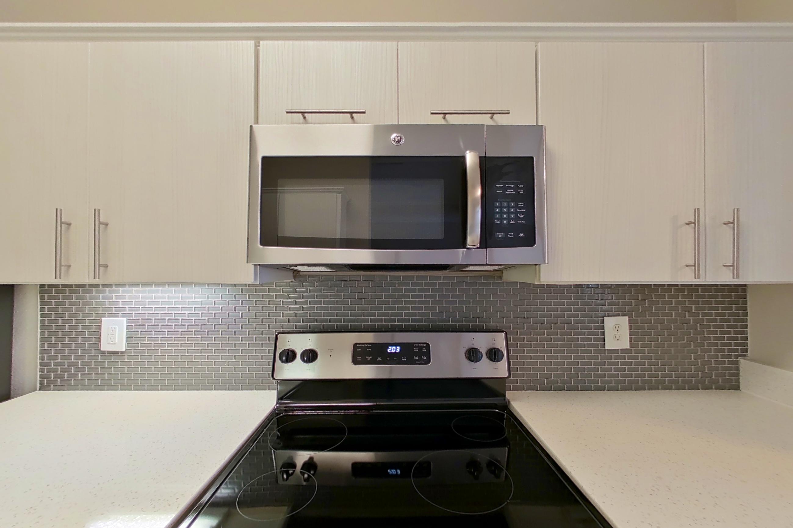 Kitchen with dishwasher, electric range, light countertops, light stone countertops, microwave, oven/range, refrigerator, and stainless steel appliances, Apartment 3508 at Marq Perimeter