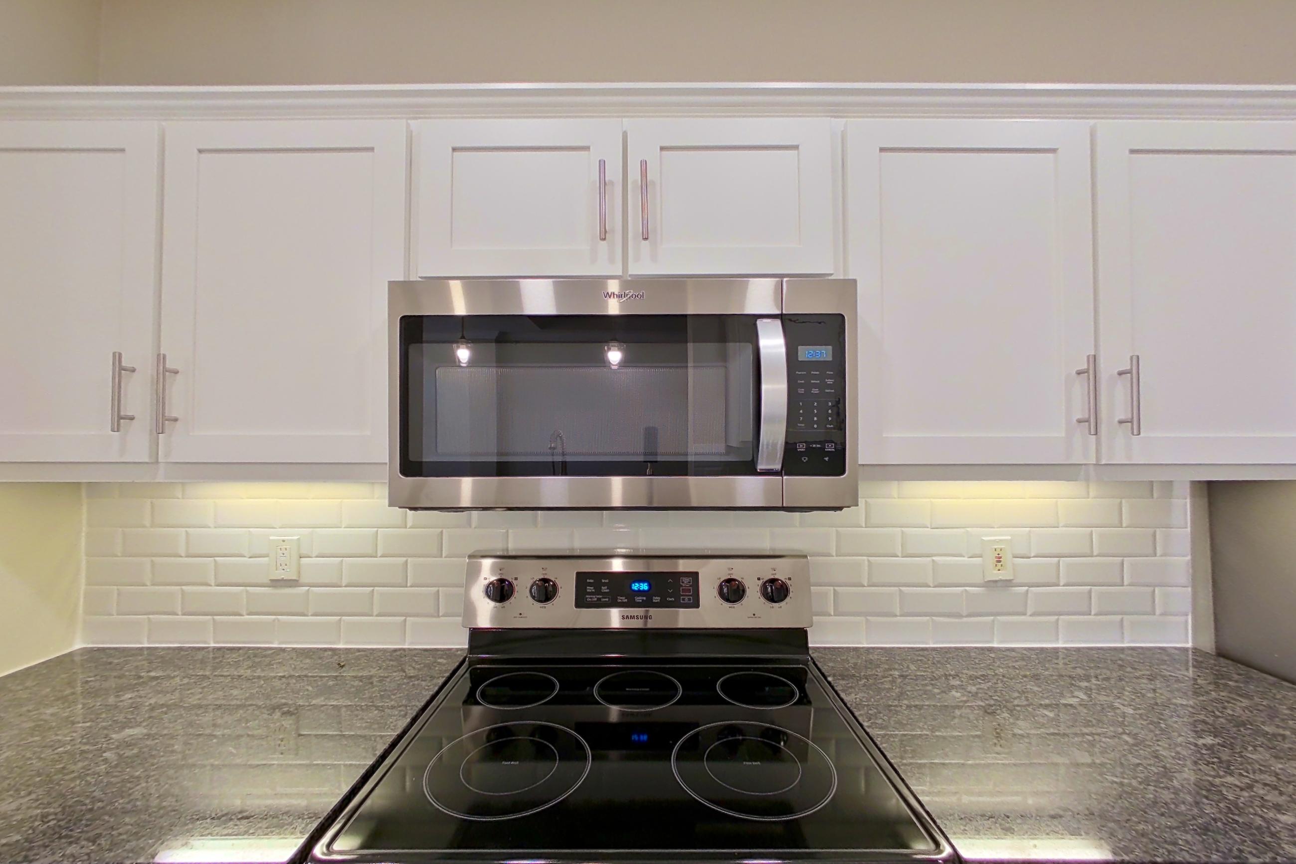 Kitchen with dark stone countertops, dishwasher, electric range, light countertops, oven/range, refrigerator, and stainless steel appliances, Apartment 3509 at Marq Perimeter