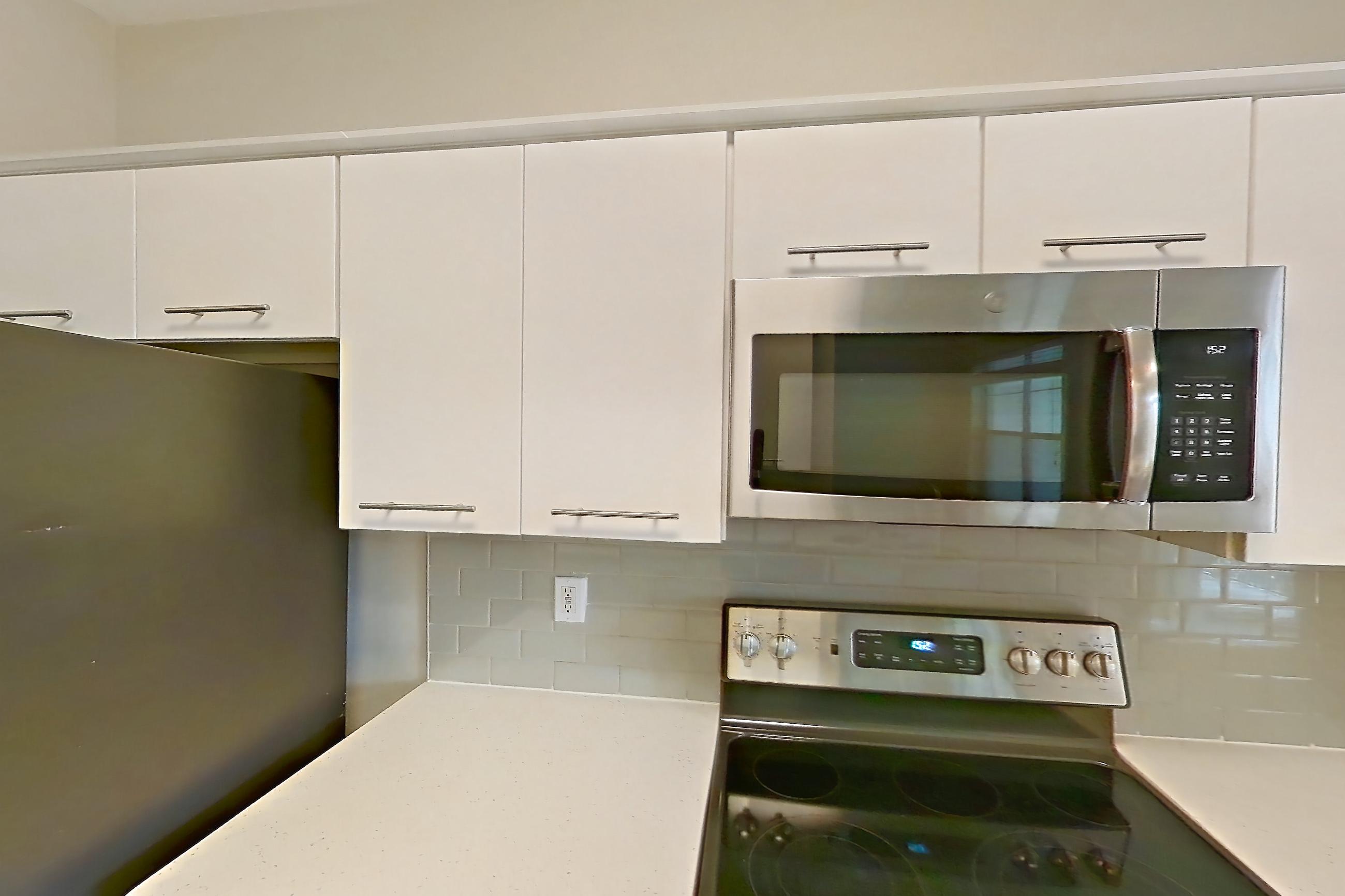 Kitchen with dark wood-finish flooring, dishwasher, electric range, light countertops, light stone countertops, microwave, oven/range, refrigerator, and stainless steel appliances, Apartment 3515 at Marq Perimeter
