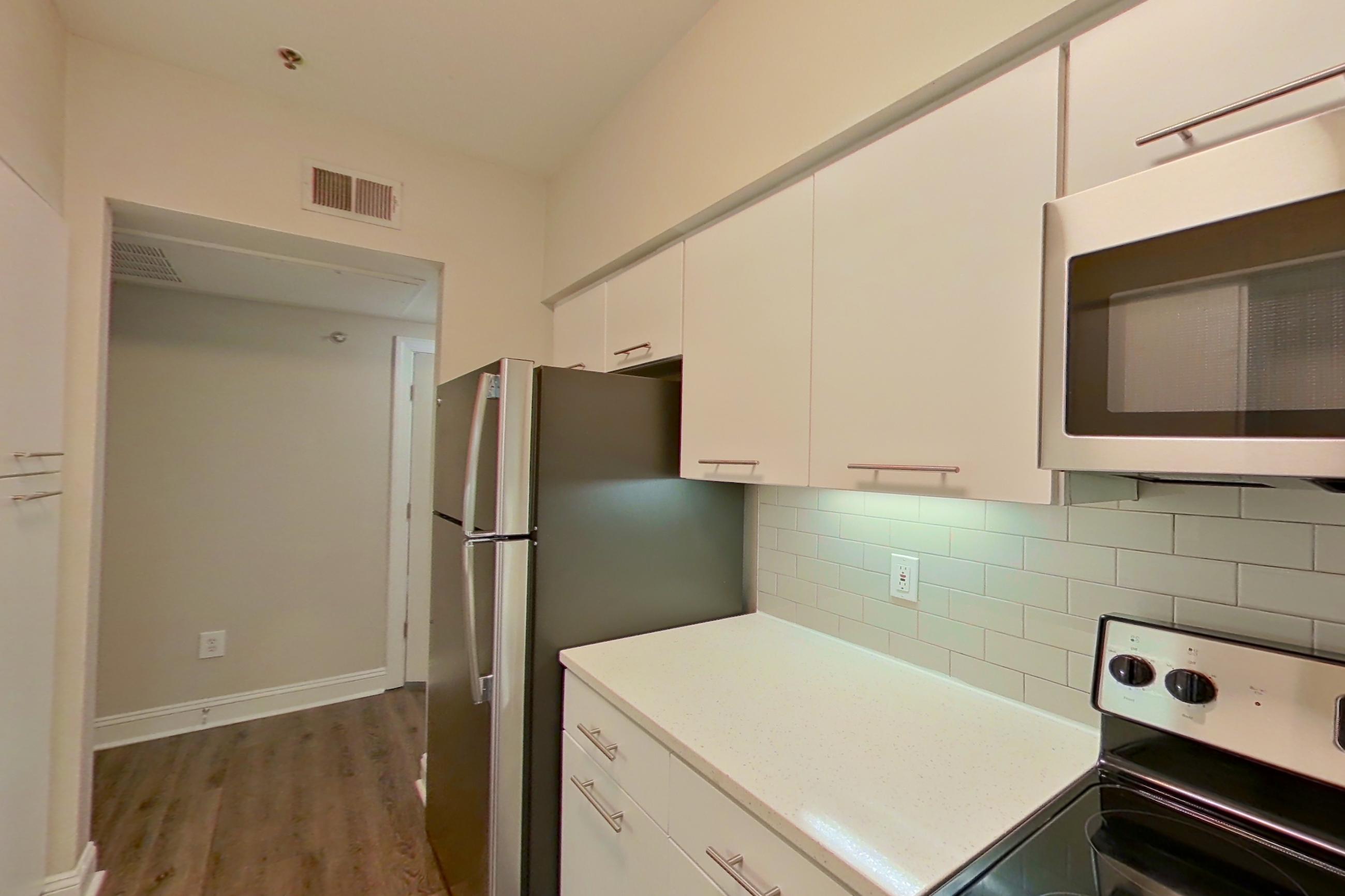 Kitchen with black appliances, dark wood-finish flooring, dishwasher, electric range, light countertops, light wood-finish flooring, microwave, oven/range, refrigerator, and stainless steel appliances, Apartment 4103 at Marq Perimeter