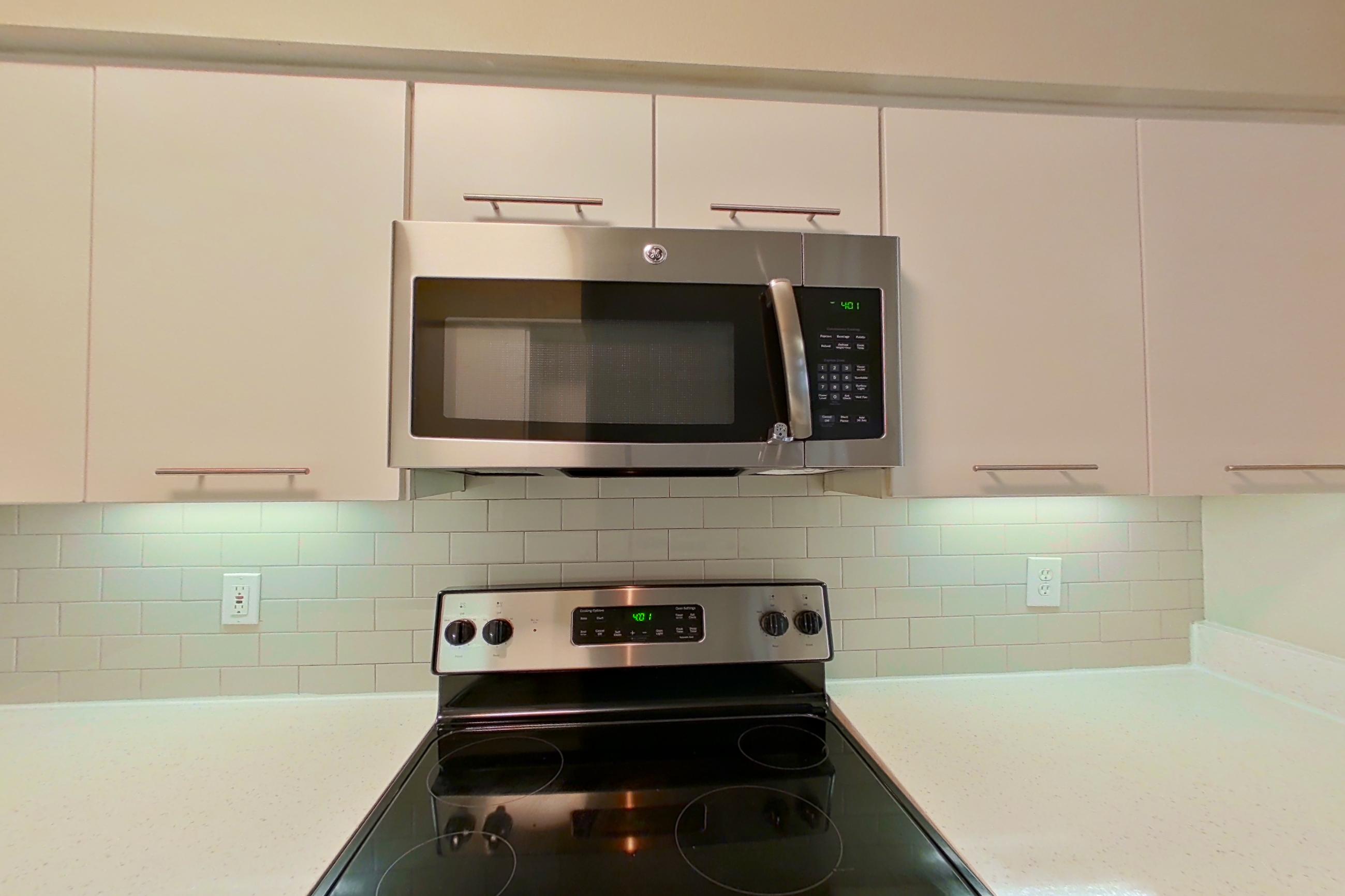Kitchen with black appliances, dark wood-finish flooring, dishwasher, electric range, light countertops, light wood-finish flooring, microwave, oven/range, refrigerator, and stainless steel appliances, Apartment 4103 at Marq Perimeter