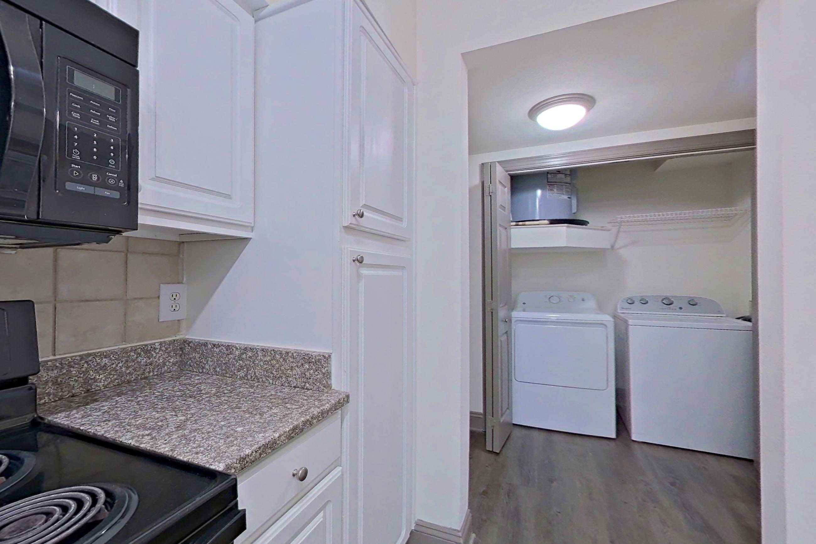 Kitchen with black appliances, electric range, in-unit laundry, light countertops, light stone countertops, microwave, oven/range, and refrigerator, Apartment 4201 at Marq Perimeter