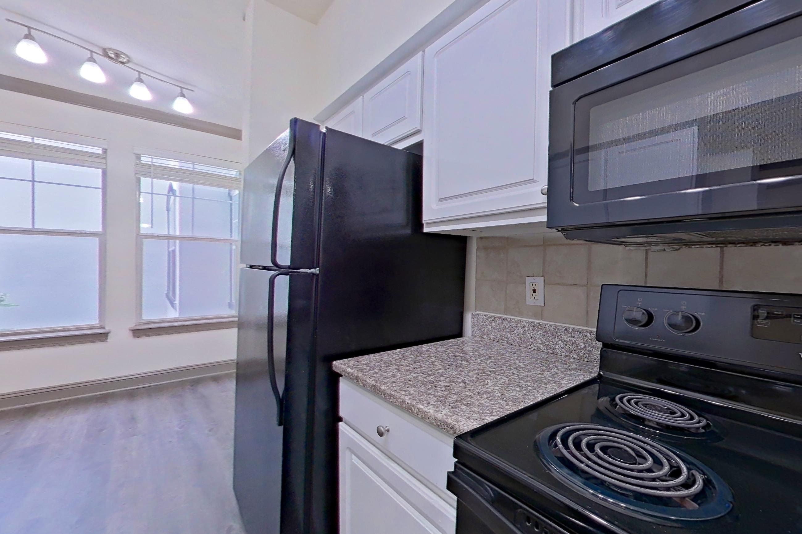 Kitchen with black appliances, electric range, in-unit laundry, light countertops, light stone countertops, microwave, oven/range, and refrigerator, Apartment 4201 at Marq Perimeter