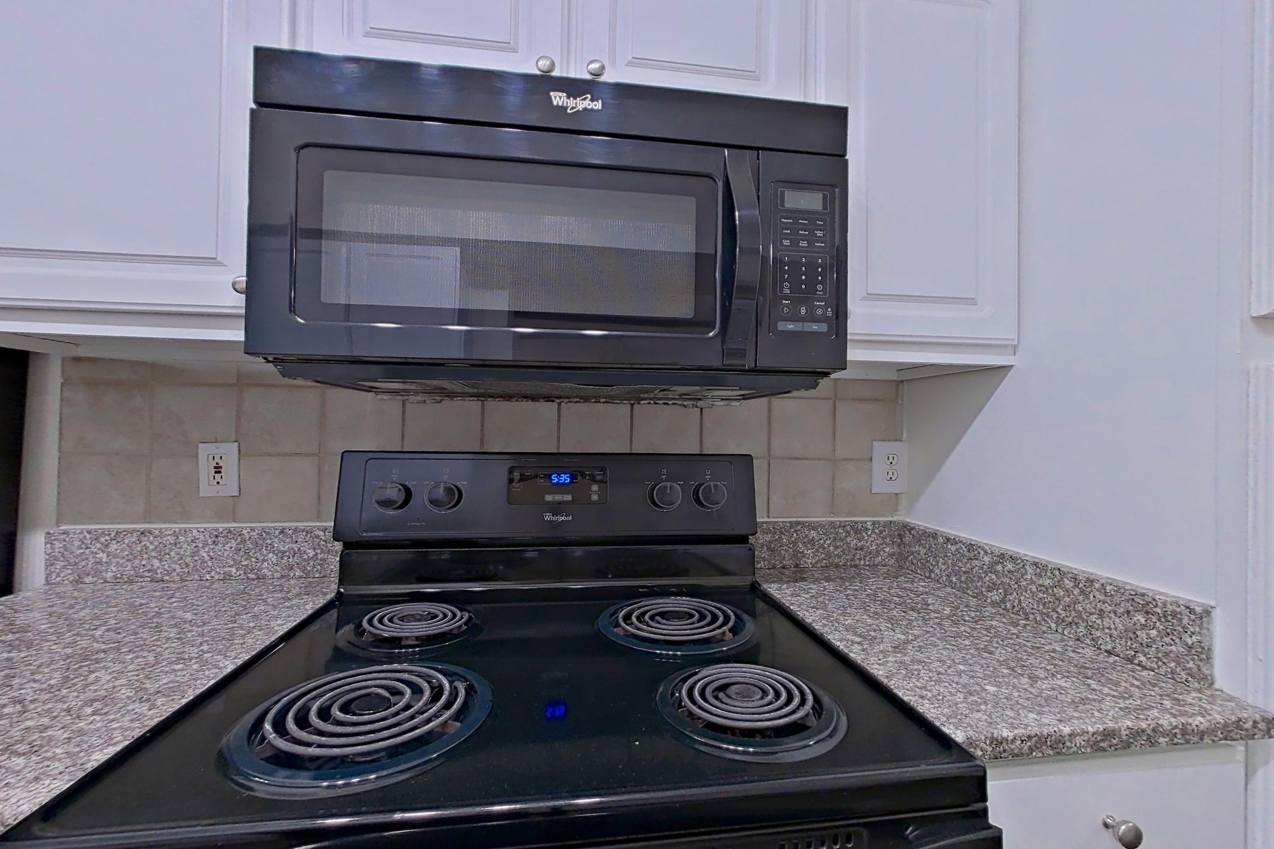 Kitchen with black appliances, electric range, in-unit laundry, light countertops, light stone countertops, microwave, oven/range, and refrigerator, Apartment 4201 at Marq Perimeter