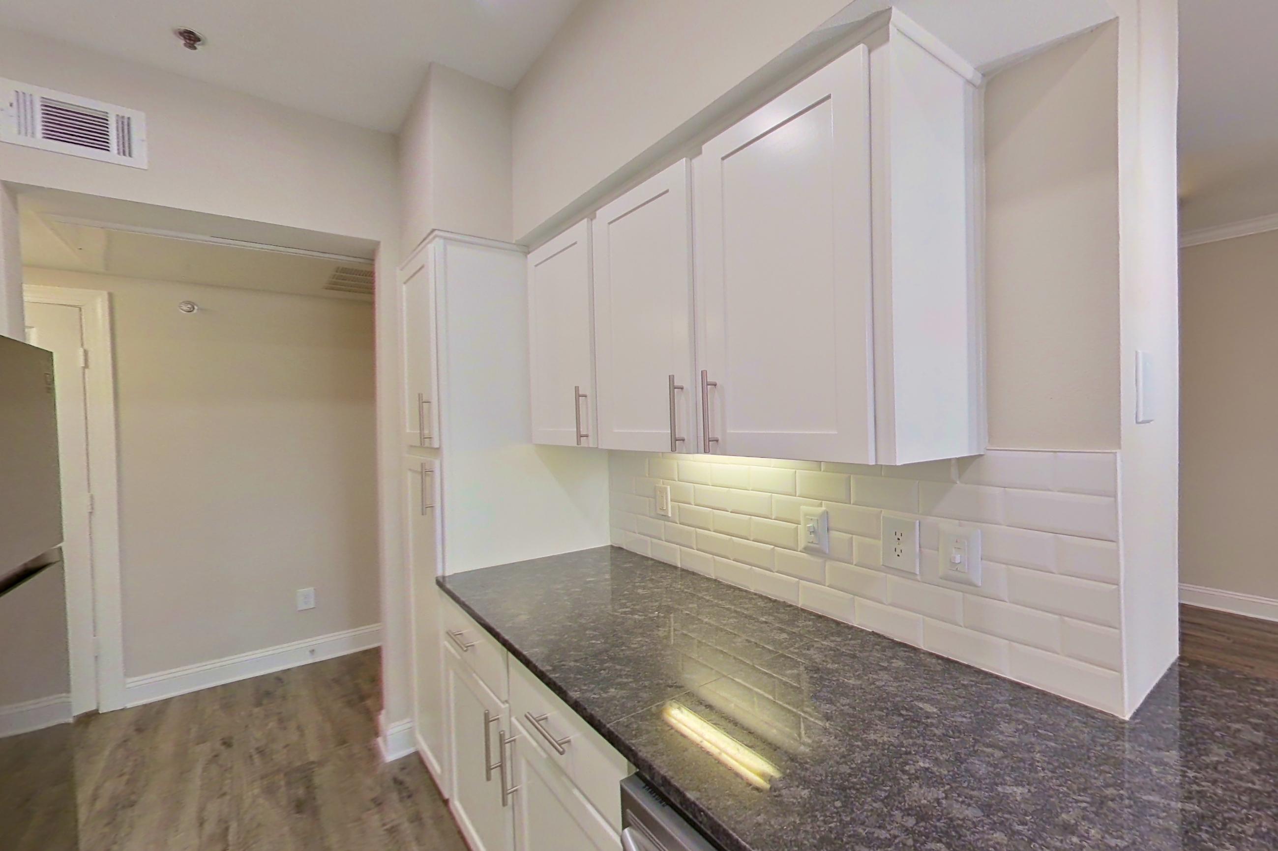 Kitchen with dark stone countertops, dishwasher, electric range, light countertops, light wood-finish flooring, oven/range, refrigerator, and stainless steel appliances, Apartment 4204 at Marq Perimeter