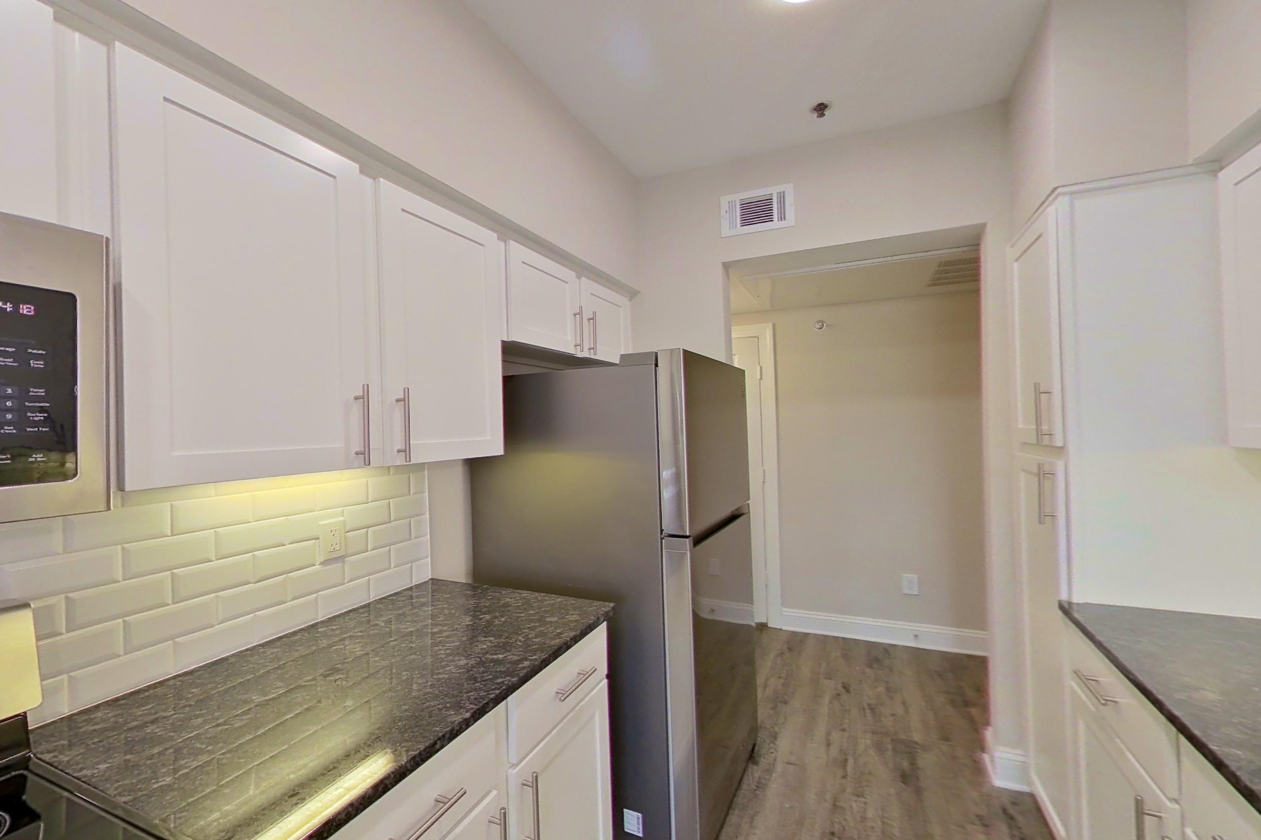 Kitchen with dark stone countertops, dishwasher, electric range, light countertops, light wood-finish flooring, oven/range, refrigerator, and stainless steel appliances, Apartment 4204 at Marq Perimeter