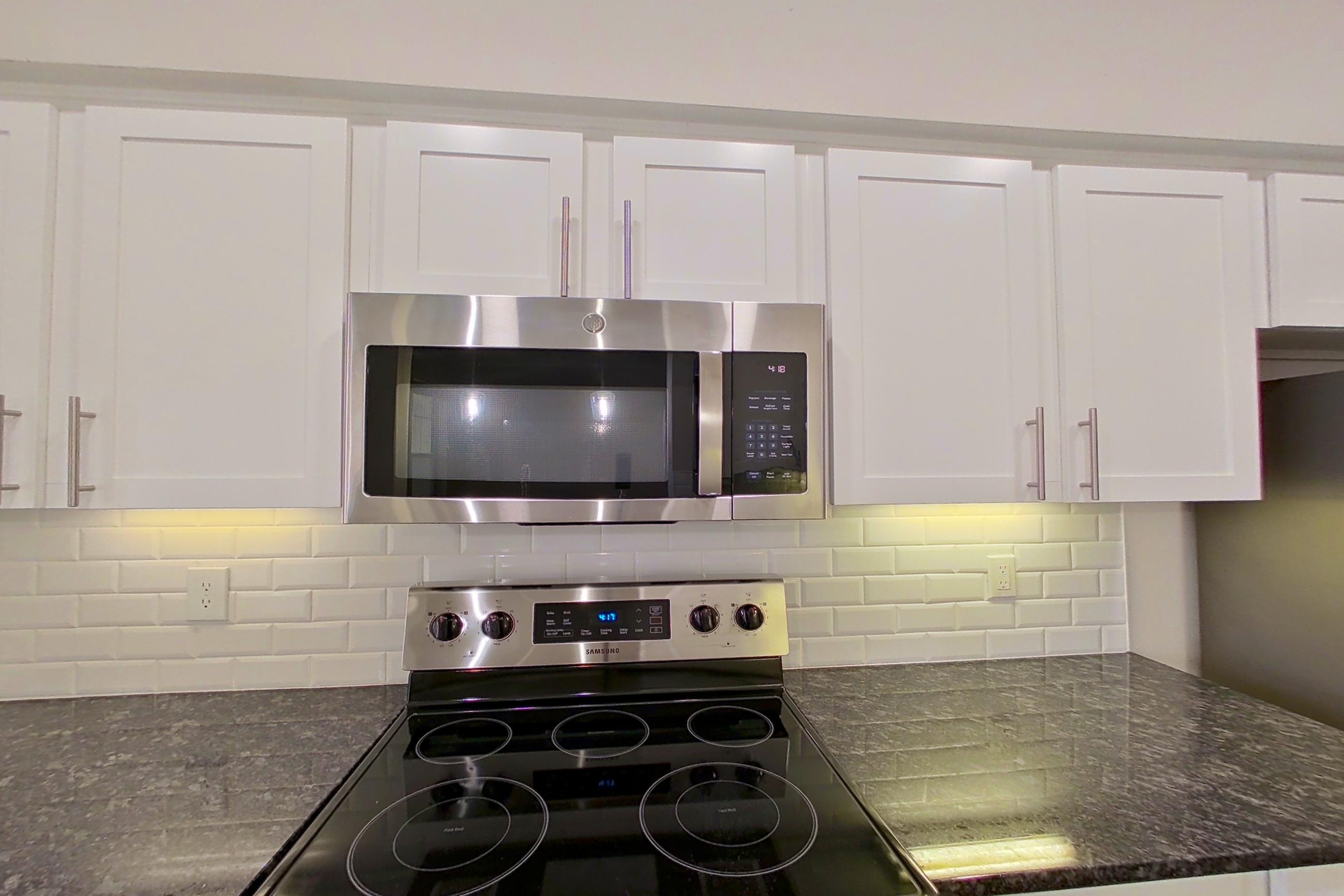 Kitchen with dark stone countertops, dishwasher, electric range, light countertops, light wood-finish flooring, oven/range, refrigerator, and stainless steel appliances, Apartment 4204 at Marq Perimeter