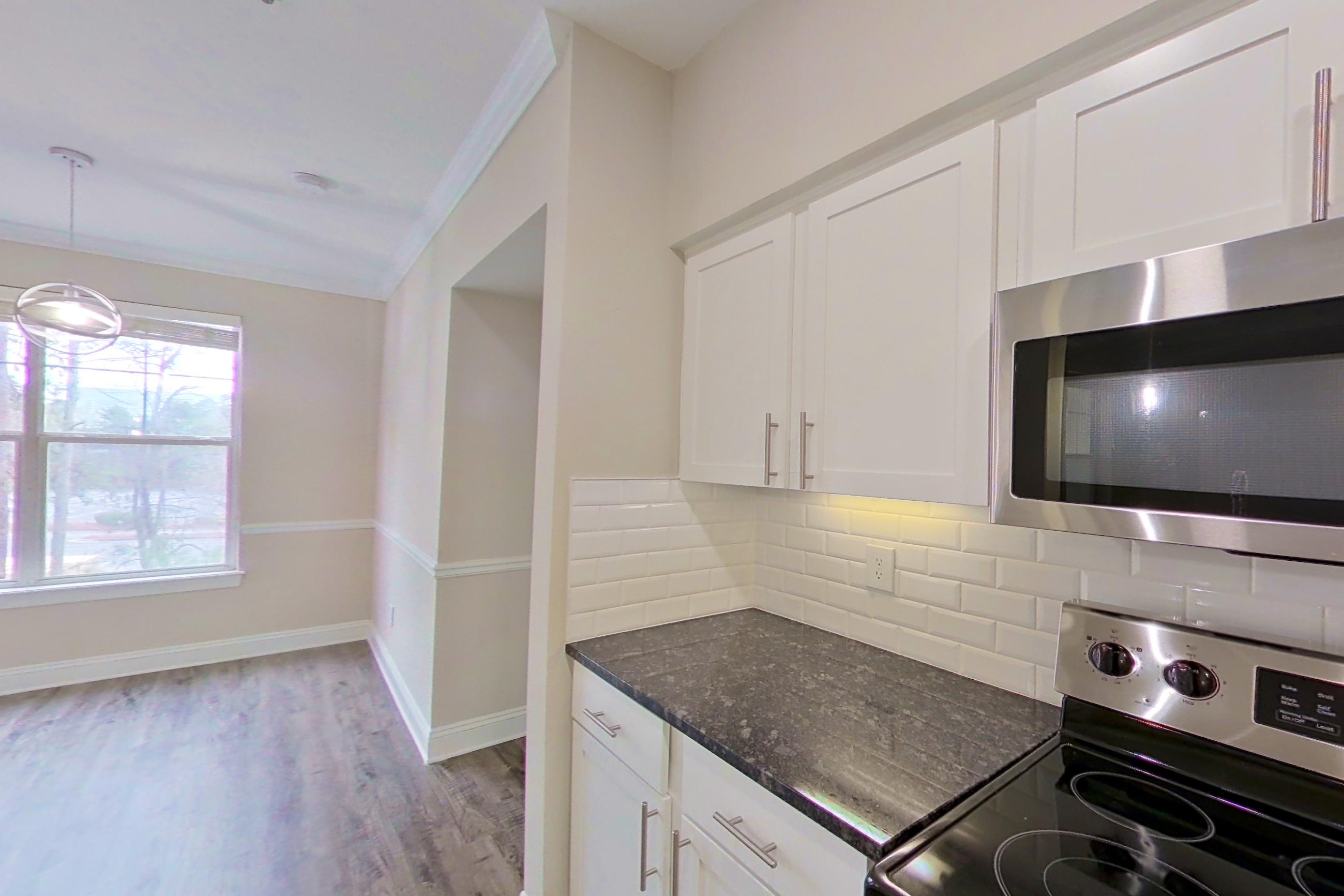 Kitchen with dark stone countertops, dishwasher, electric range, light countertops, light wood-finish flooring, oven/range, refrigerator, and stainless steel appliances, Apartment 4204 at Marq Perimeter