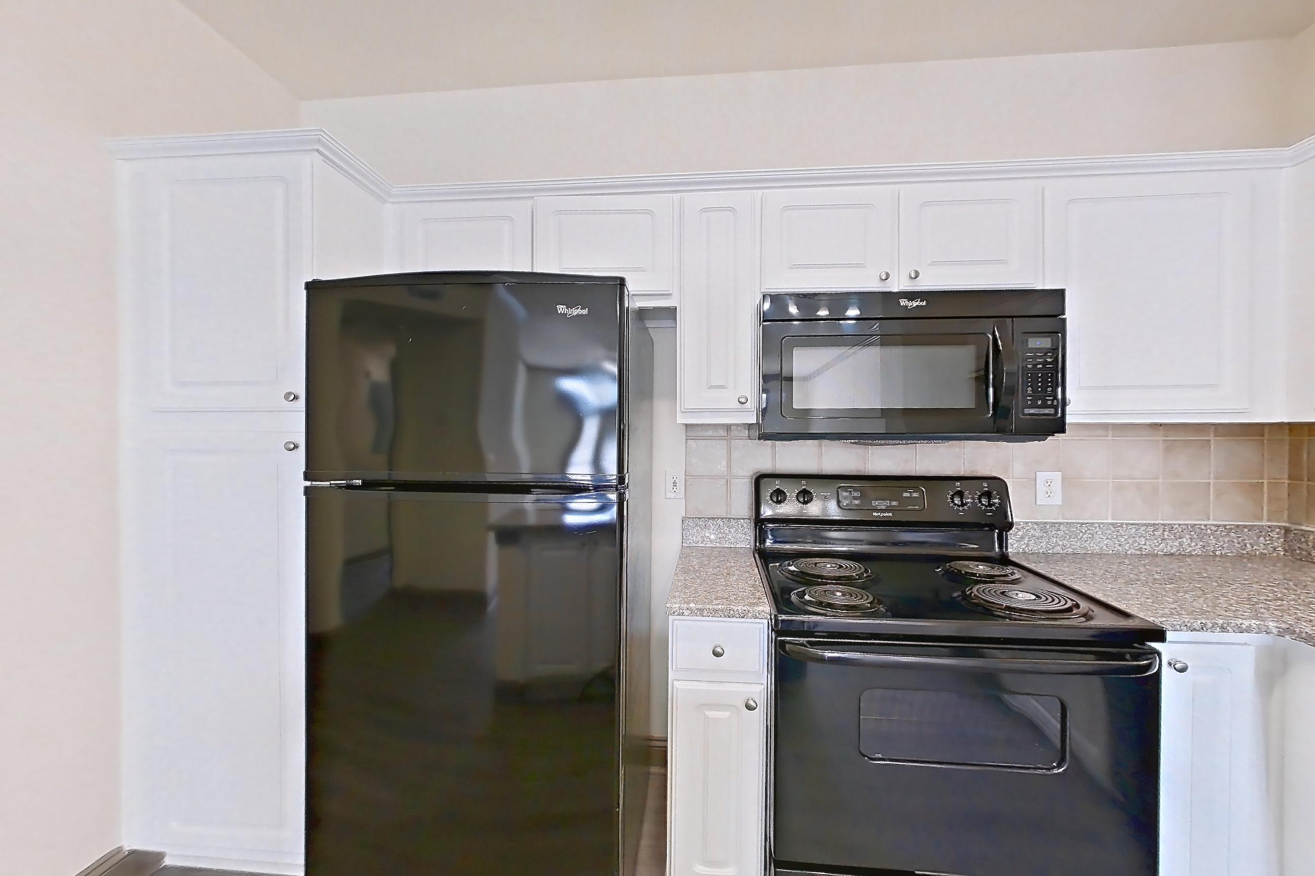 Kitchen with black appliances, dishwasher, electric range, light countertops, light stone countertops, light wood-finish flooring, microwave, and oven/range, Apartment 4208 at Marq Perimeter