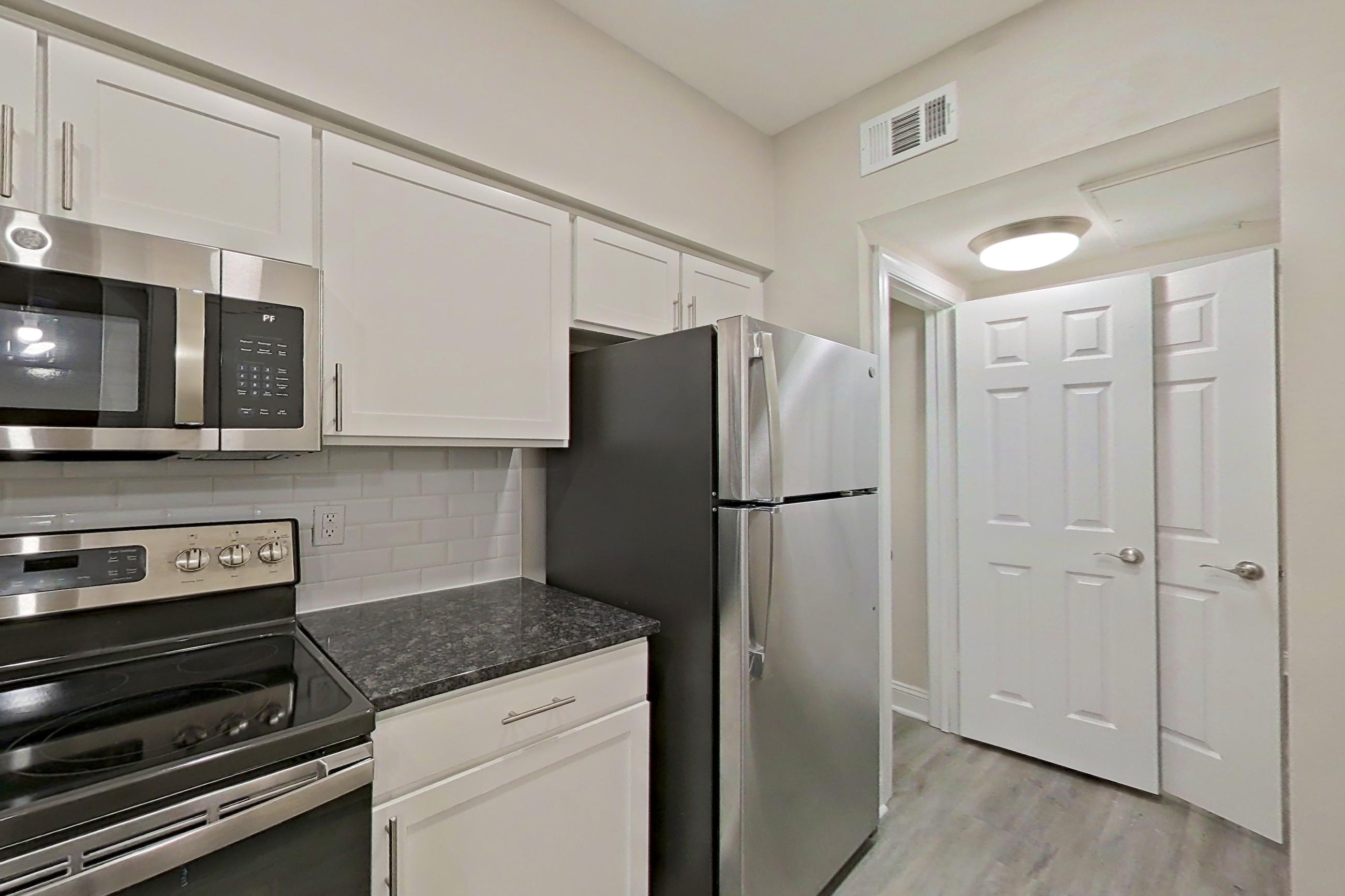 Kitchen with dark stone countertops, electric range, light countertops, light wood-finish flooring, microwave, oven/range, refrigerator, and stainless steel appliances, Apartment 4213 at Marq Perimeter