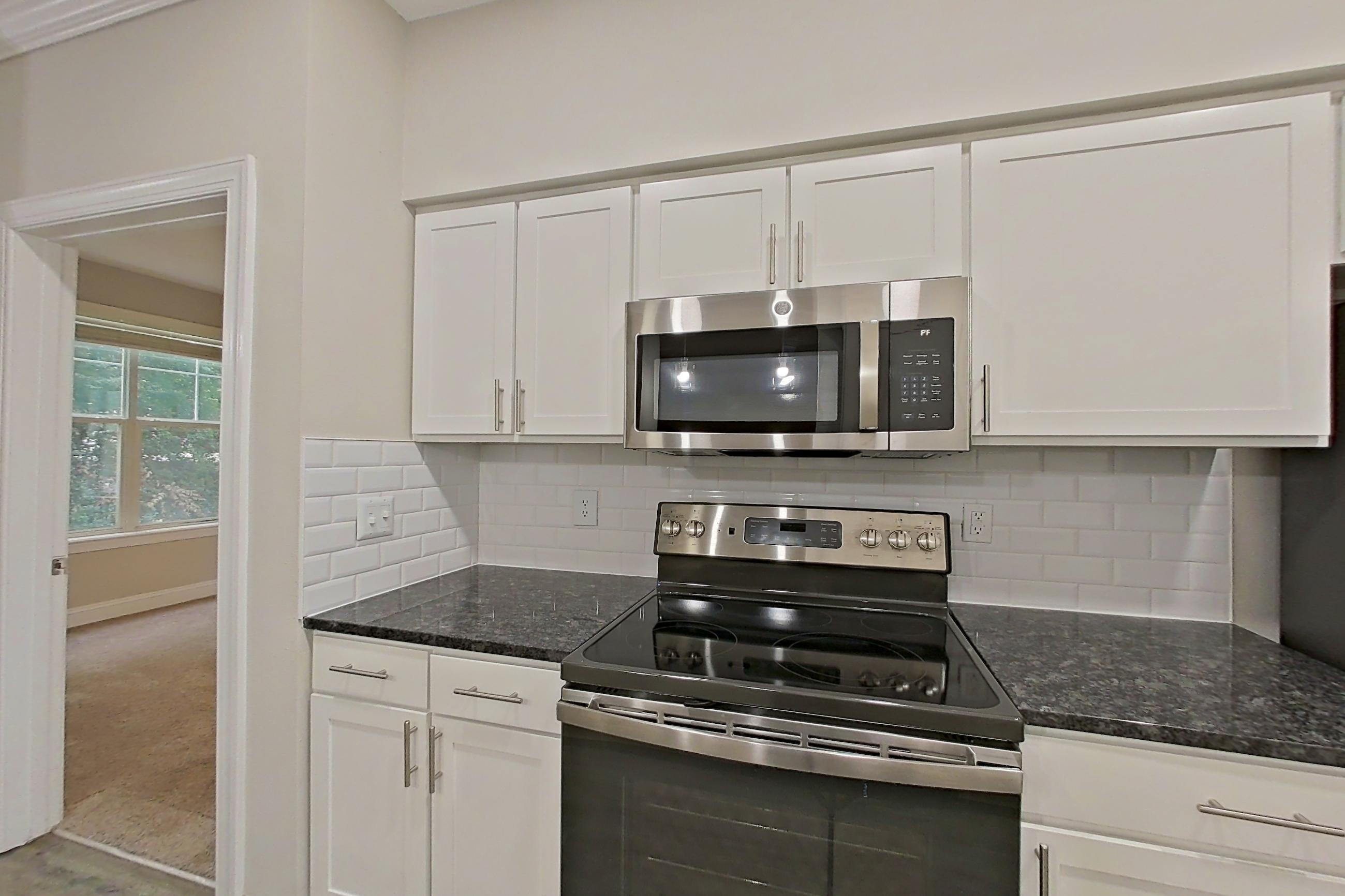 Kitchen with dark stone countertops, electric range, light countertops, light wood-finish flooring, microwave, oven/range, refrigerator, and stainless steel appliances, Apartment 4213 at Marq Perimeter