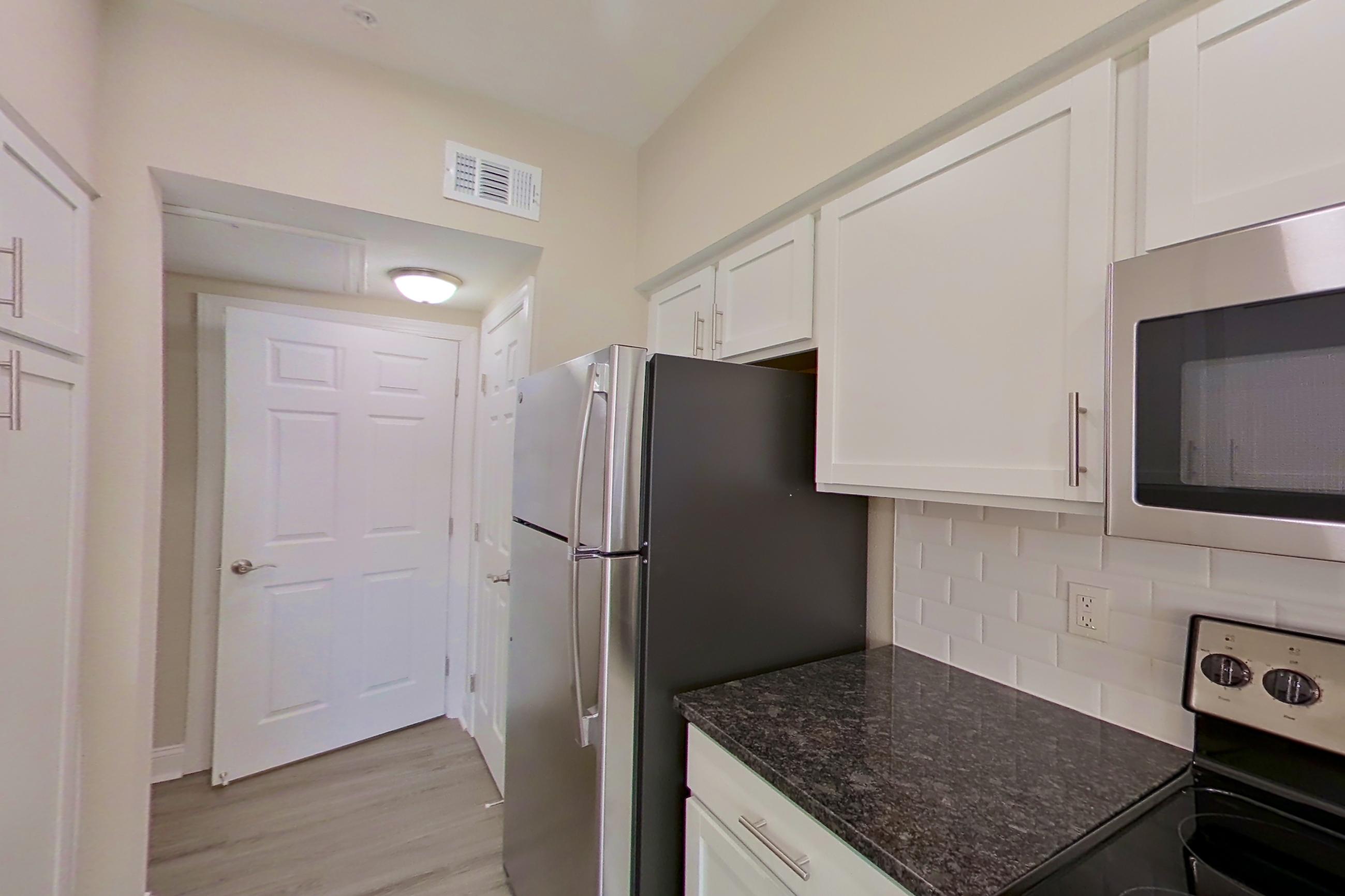 Kitchen with dark stone countertops, electric range, light countertops, light wood-finish flooring, microwave, oven/range, refrigerator, and stainless steel appliances, Apartment 4214 at Marq Perimeter