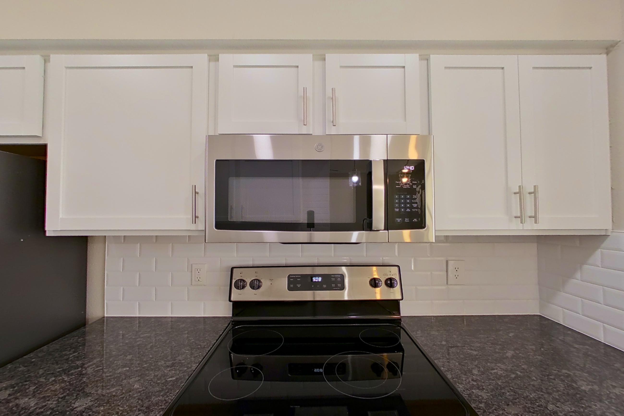 Kitchen with dark stone countertops, electric range, light countertops, light wood-finish flooring, microwave, oven/range, refrigerator, and stainless steel appliances, Apartment 4214 at Marq Perimeter