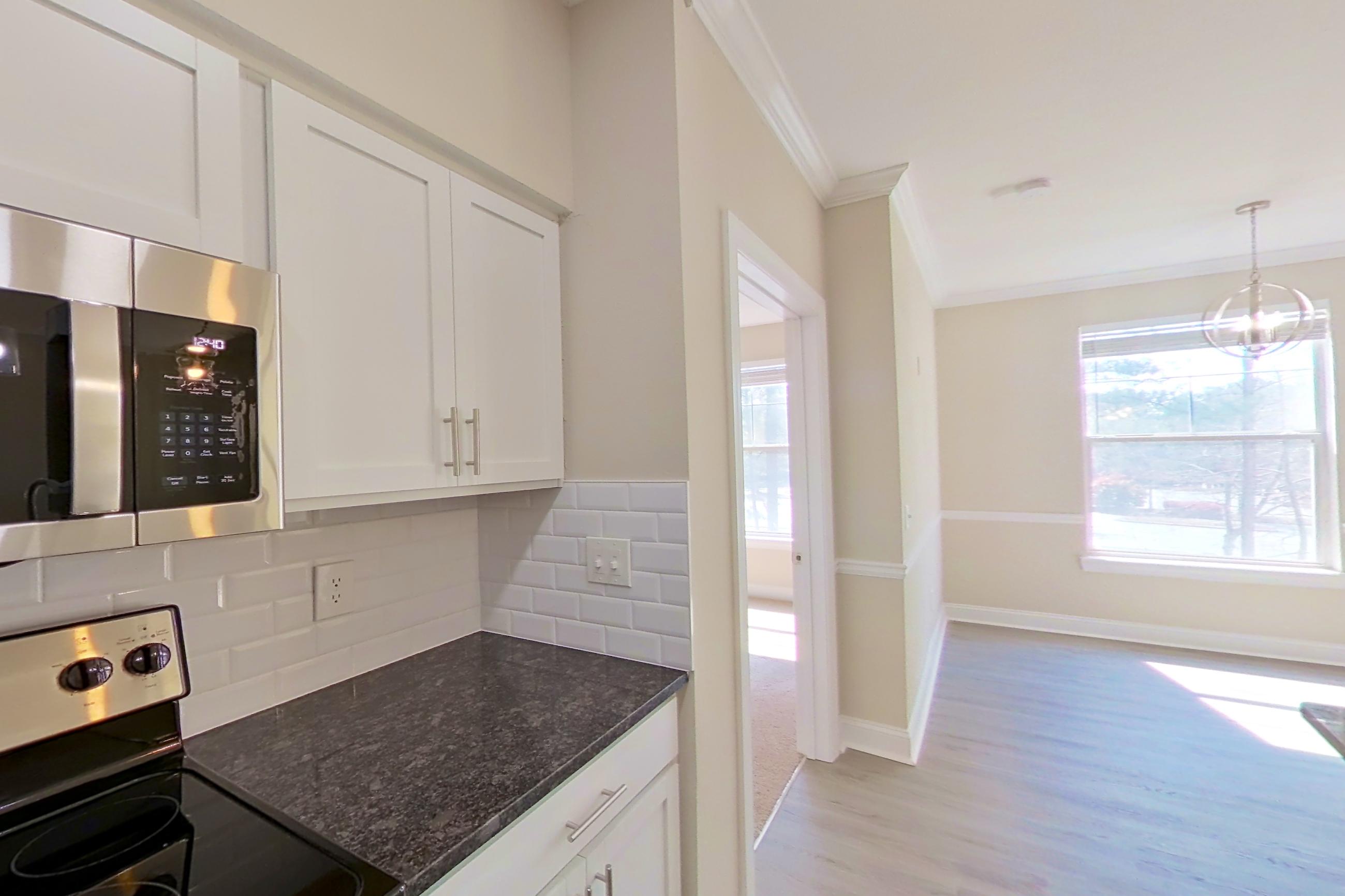 Kitchen with dark stone countertops, electric range, light countertops, light wood-finish flooring, microwave, oven/range, refrigerator, and stainless steel appliances, Apartment 4214 at Marq Perimeter