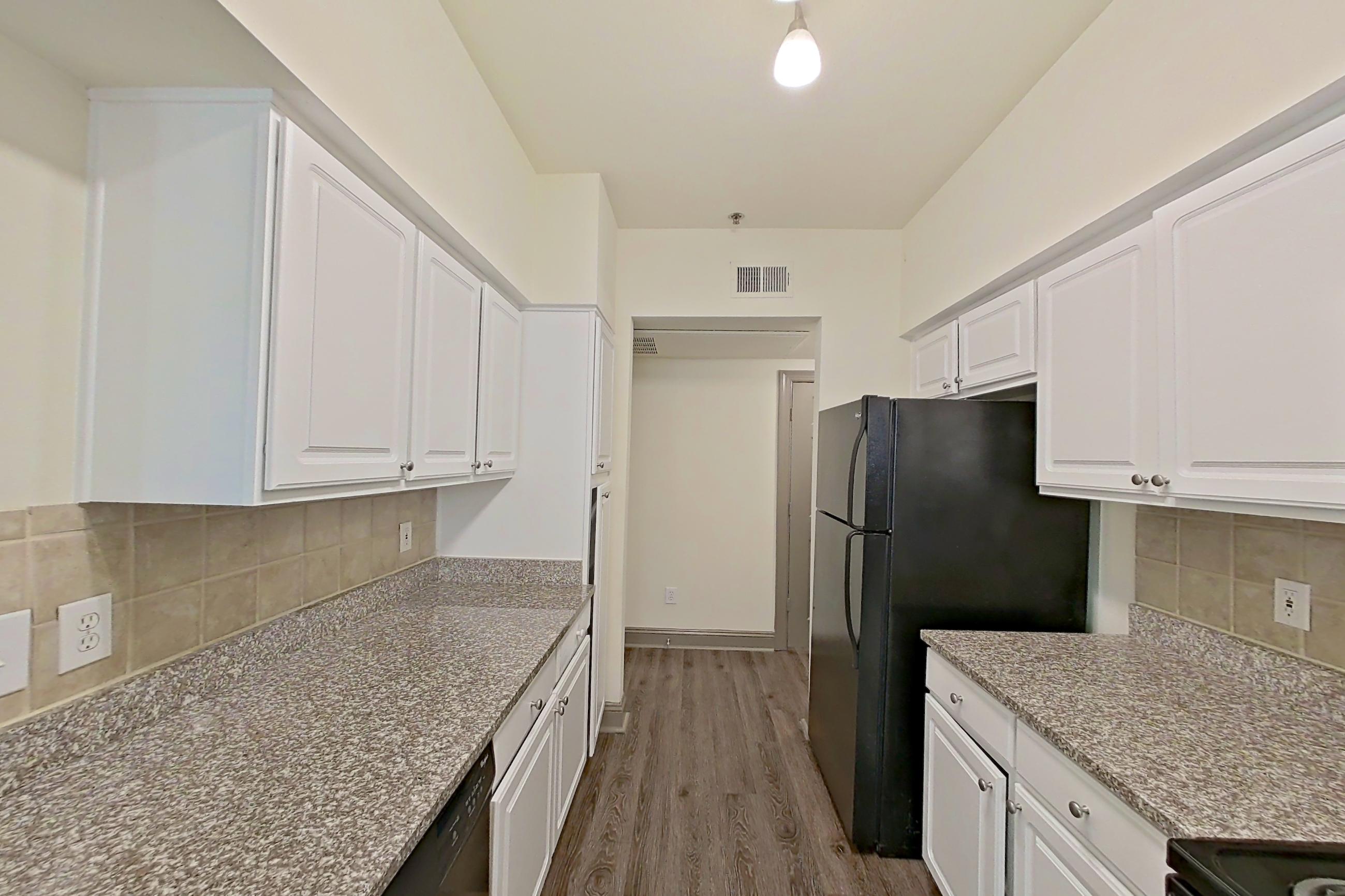 Kitchen with black appliances, dark stone countertops, dark wood-finish flooring, dishwasher, electric range, light countertops, light stone countertops, microwave, oven/range, refrigerator, and stainless steel appliances, Apartment 4303 at Marq Perimeter