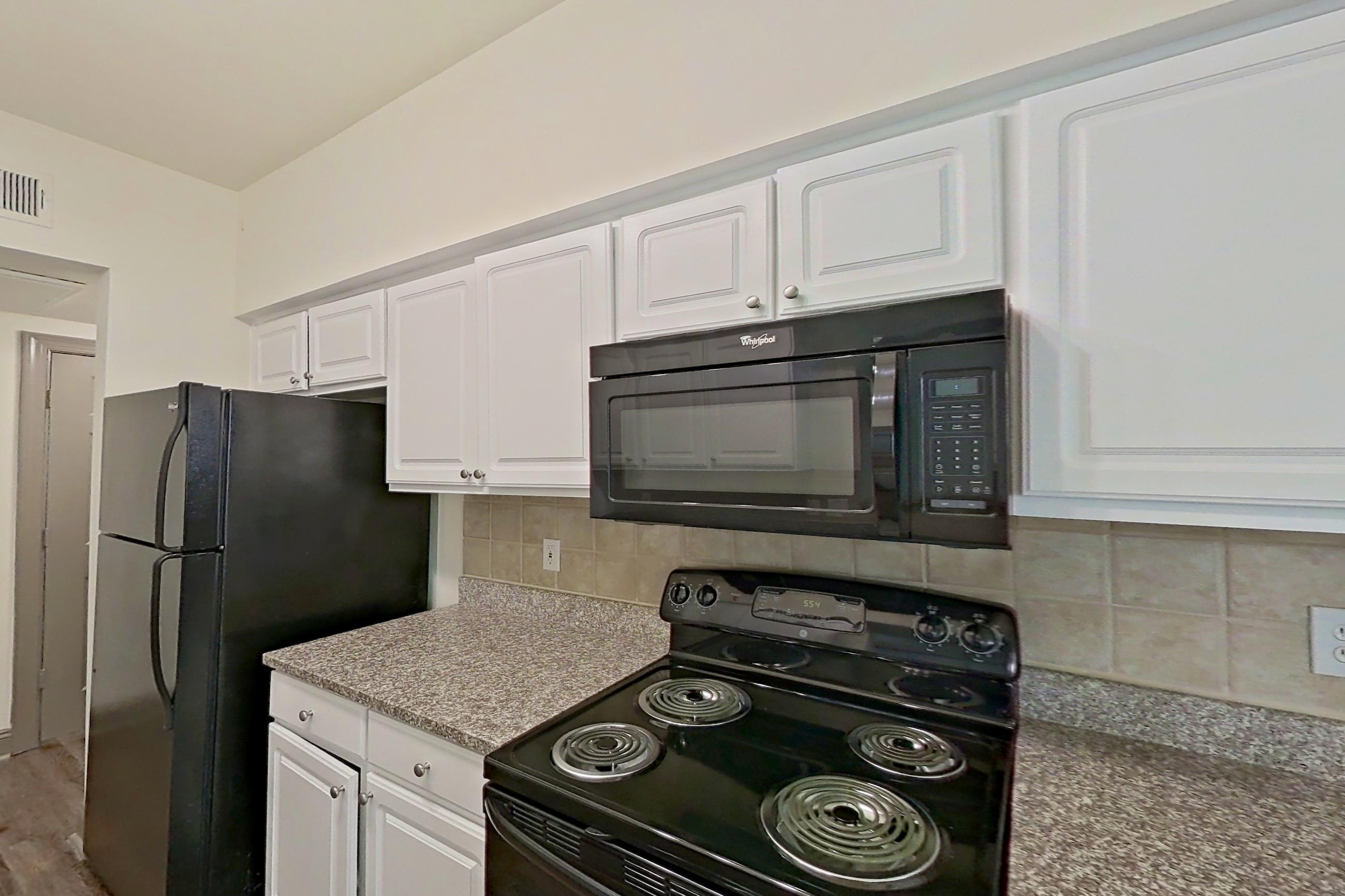 Kitchen with black appliances, dark stone countertops, dark wood-finish flooring, dishwasher, electric range, light countertops, light stone countertops, microwave, oven/range, refrigerator, and stainless steel appliances, Apartment 4303 at Marq Perimeter