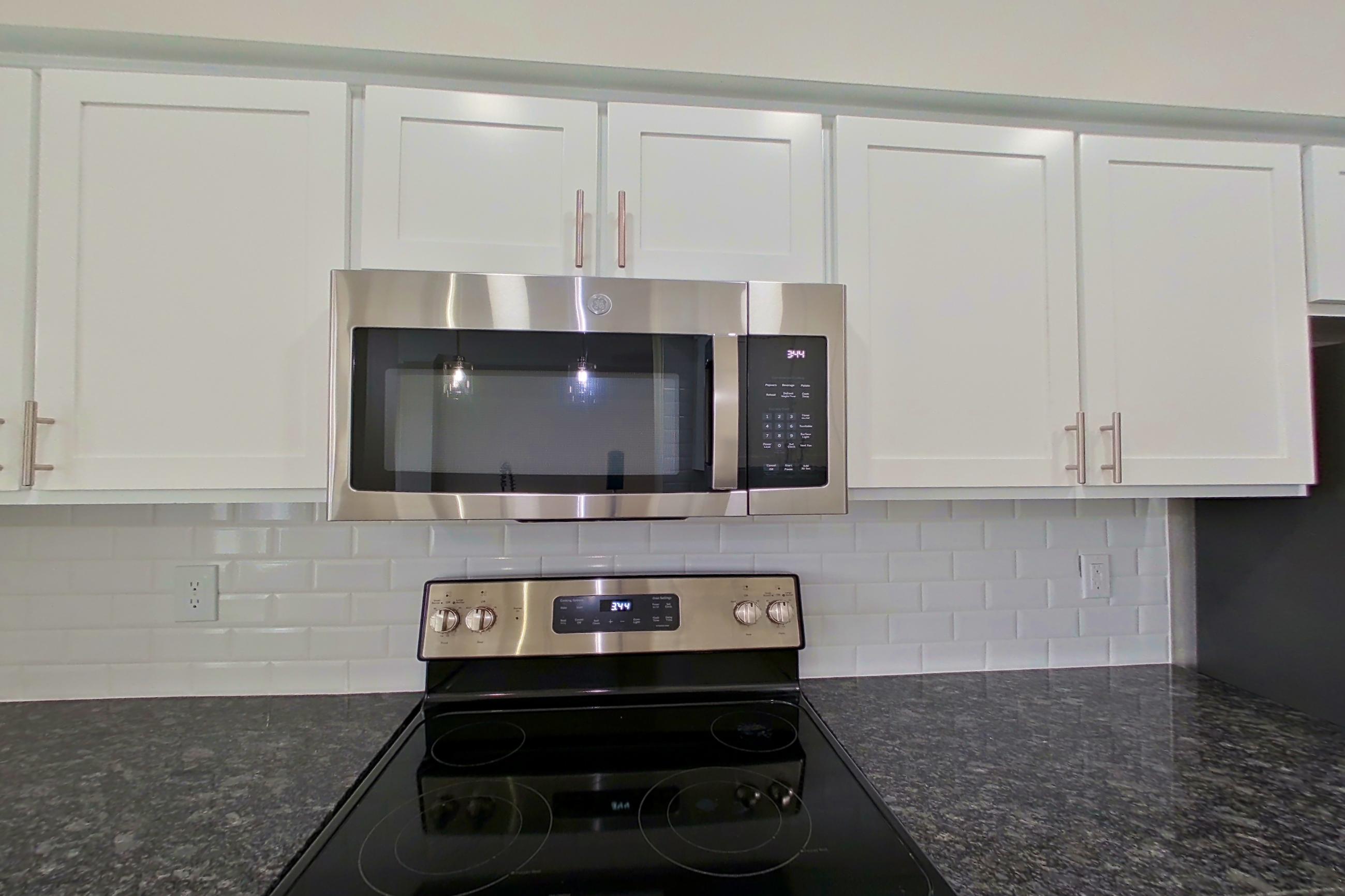 Kitchen with dark stone countertops, electric range, light countertops, light wood-finish flooring, microwave, oven/range, refrigerator, and stainless steel appliances, Apartment 4304 at Marq Perimeter