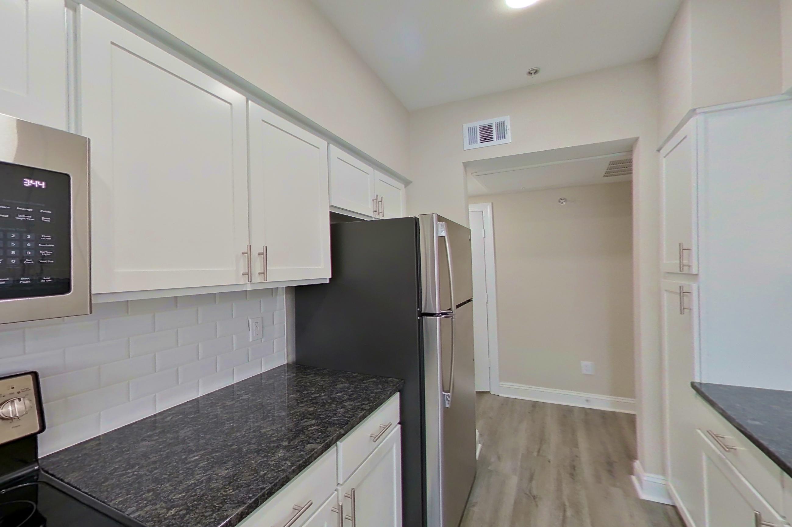 Kitchen with dark stone countertops, electric range, light countertops, light wood-finish flooring, microwave, oven/range, refrigerator, and stainless steel appliances, Apartment 4304 at Marq Perimeter