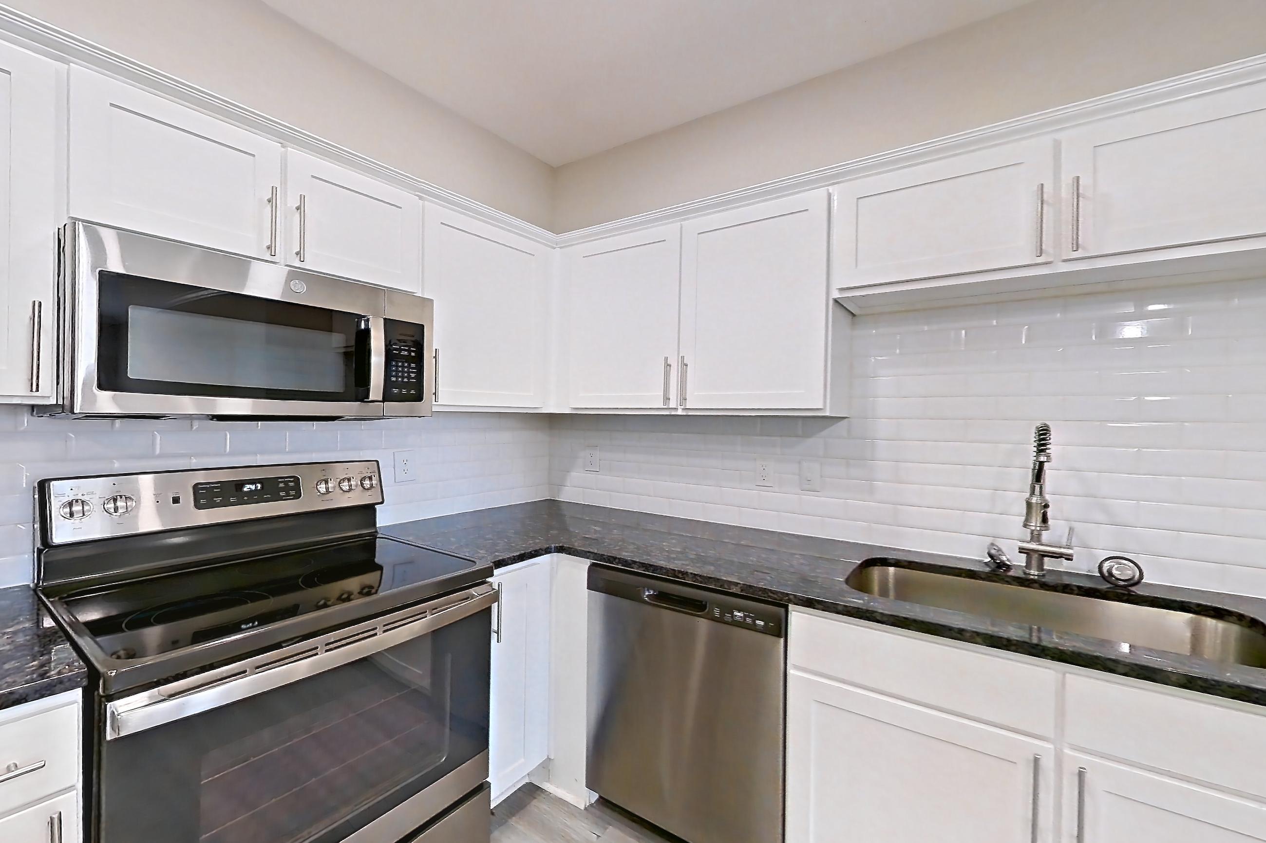 Kitchen with dark stone countertops, dishwasher, electric range, light countertops, light wood-finish flooring, microwave, oven/range, refrigerator, and stainless steel appliances, Apartment 4312 at Marq Perimeter