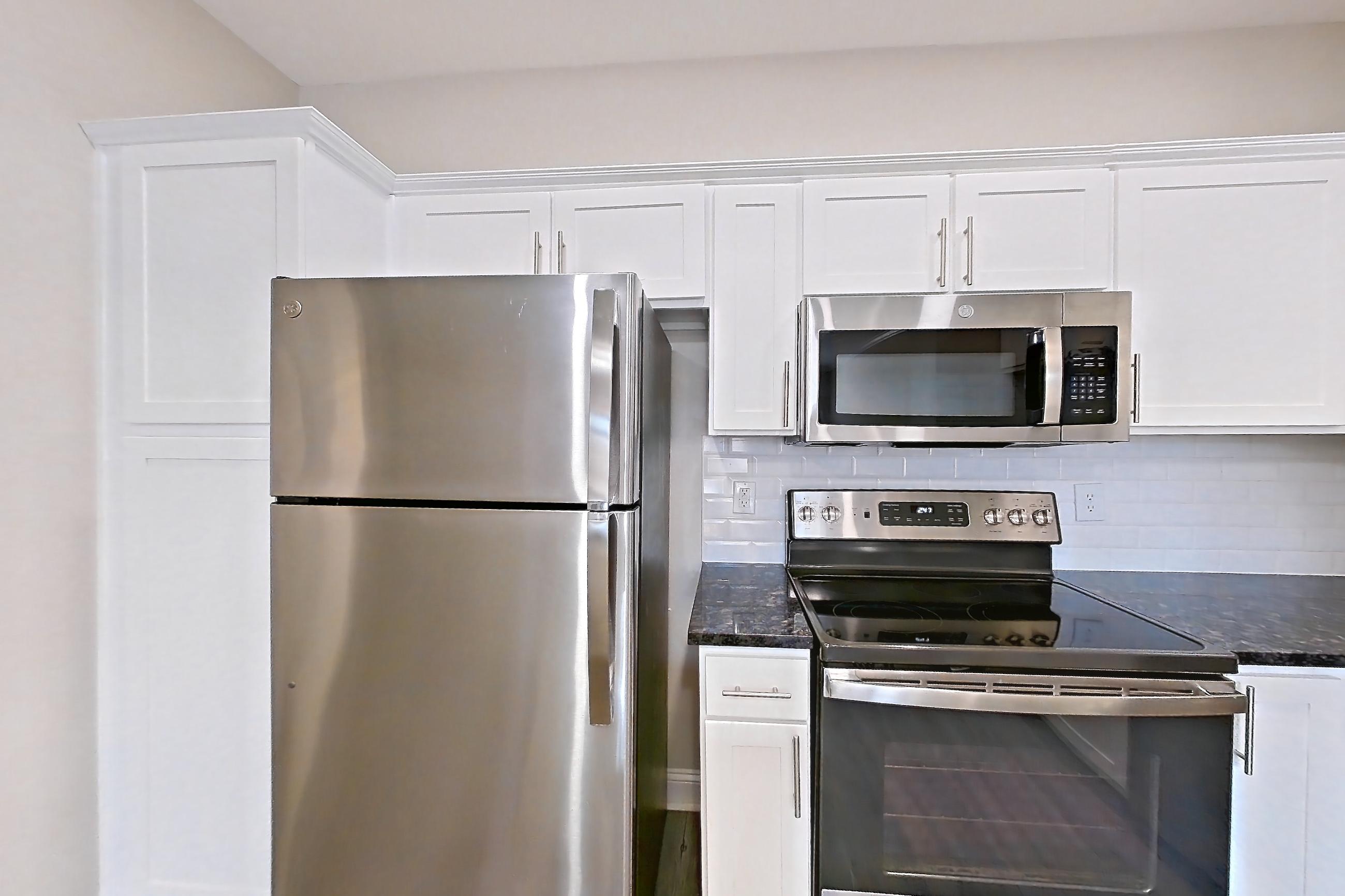 Kitchen with dark stone countertops, dishwasher, electric range, light countertops, light wood-finish flooring, microwave, oven/range, refrigerator, and stainless steel appliances, Apartment 4312 at Marq Perimeter