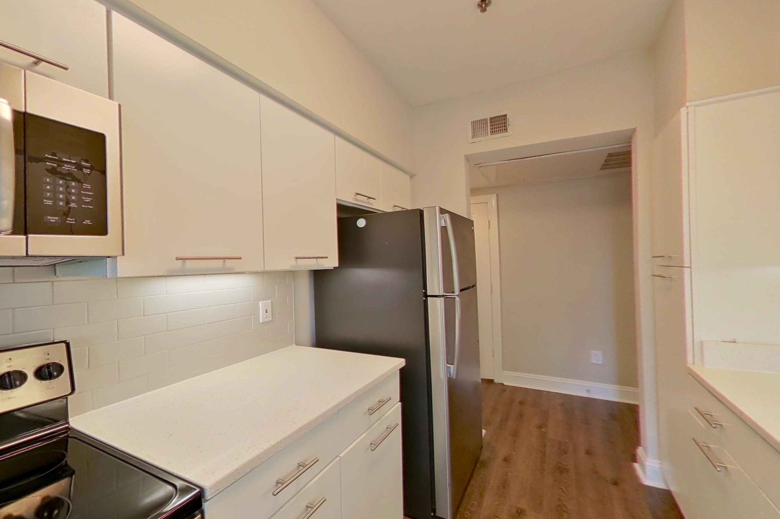 Kitchen with dark wood-finish flooring, dishwasher, electric range, light countertops, light stone countertops, light wood-finish flooring, microwave, oven/range, refrigerator, and stainless steel appliances, Apartment 4404 at Marq Perimeter
