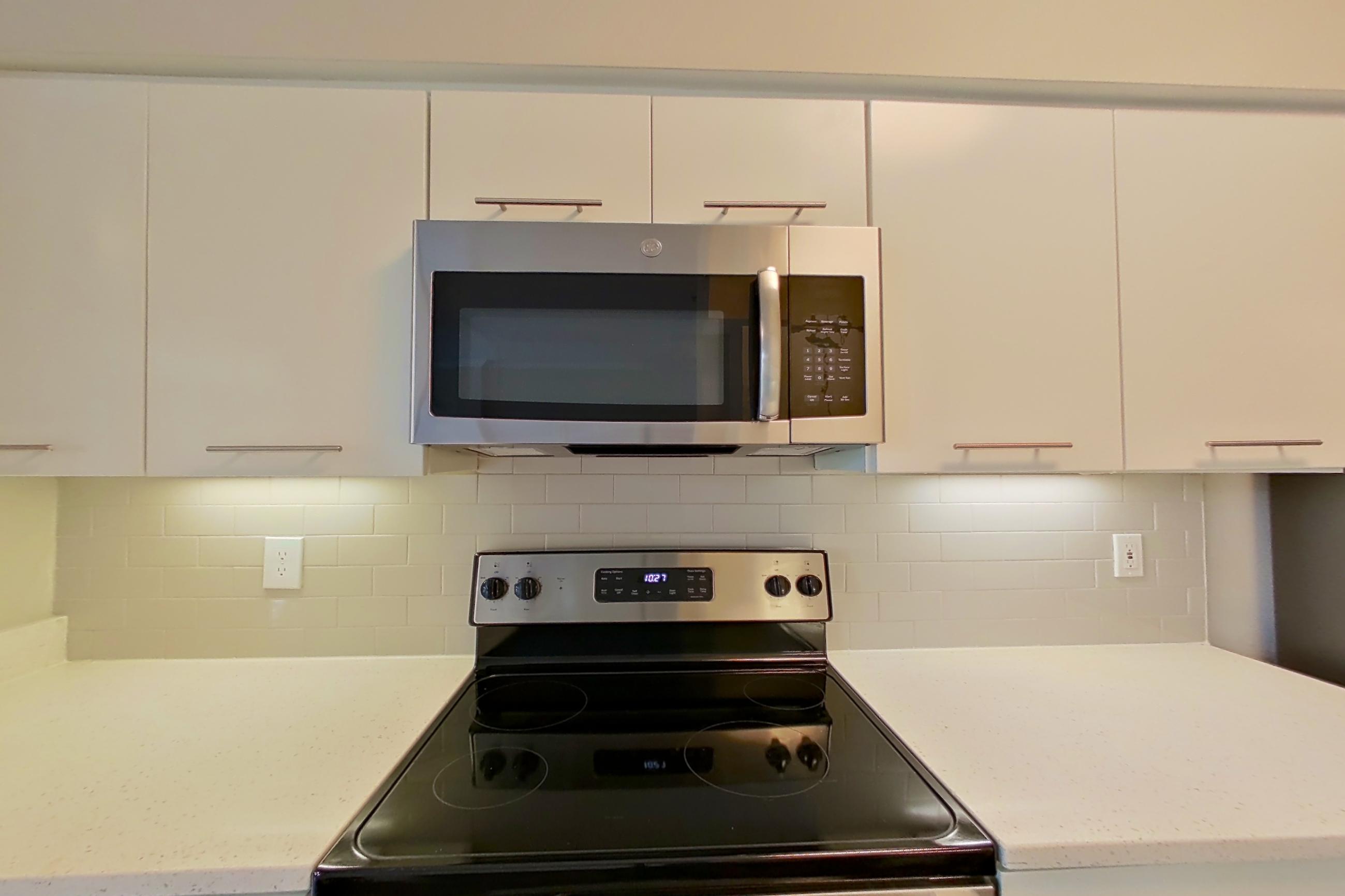 Kitchen with dark wood-finish flooring, dishwasher, electric range, light countertops, light stone countertops, light wood-finish flooring, microwave, oven/range, refrigerator, and stainless steel appliances, Apartment 4404 at Marq Perimeter