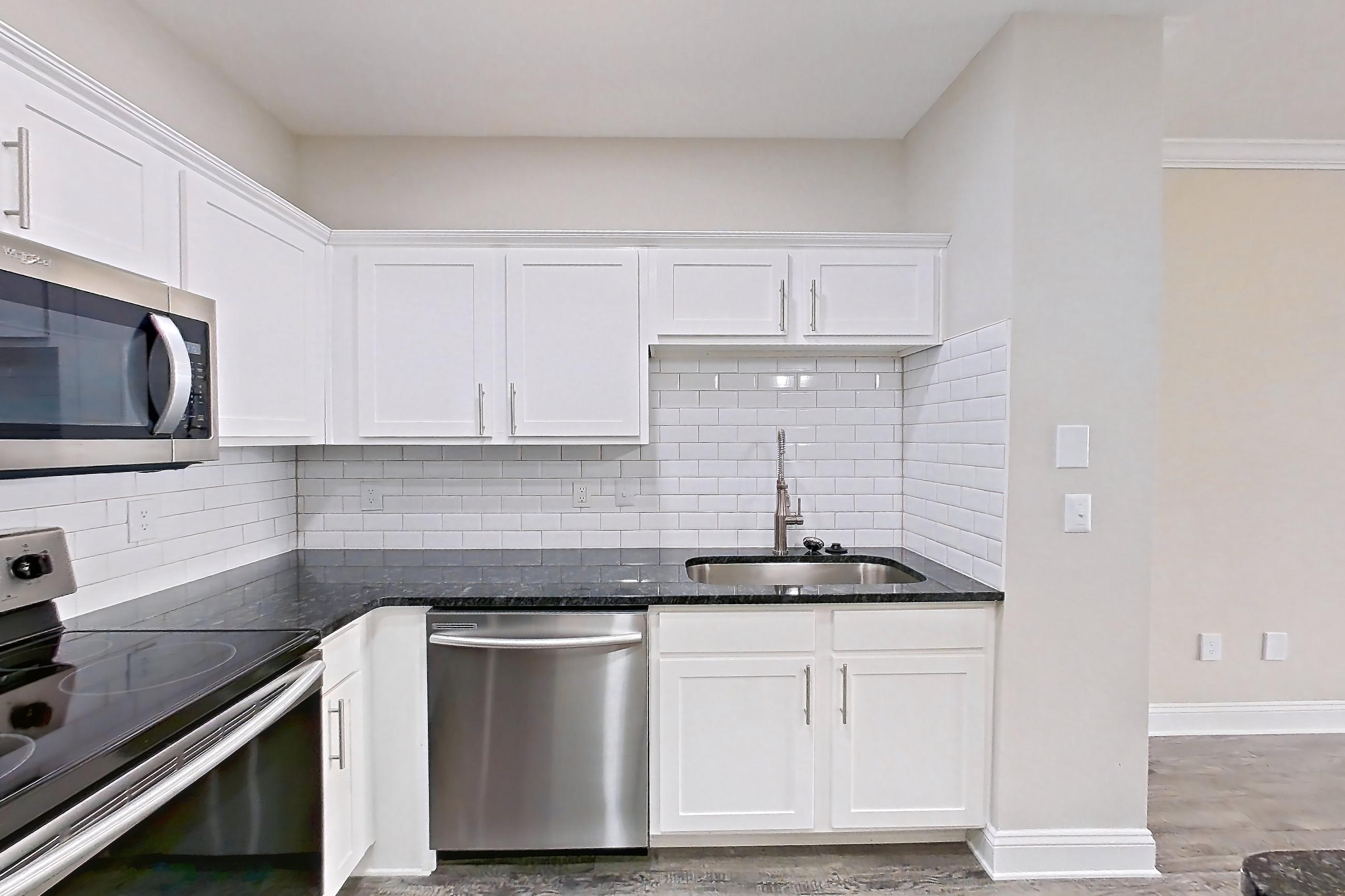 Kitchen with dark countertops, dark stone countertops, dishwasher, electric range, light wood-finish flooring, oven/range, refrigerator, and stainless steel appliances, Apartment 4309 at Marq Perimeter