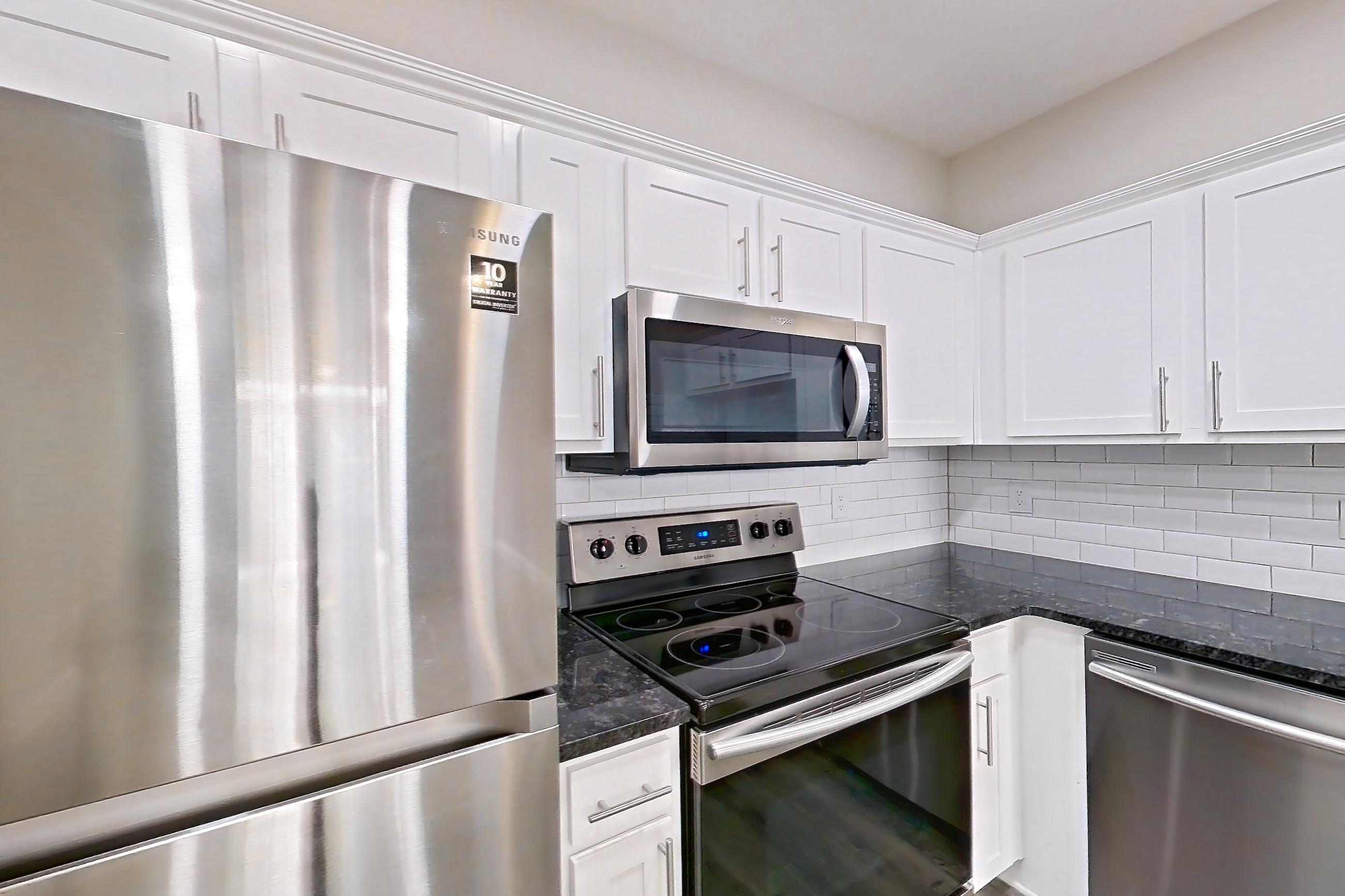 Kitchen with dark countertops, dark stone countertops, dishwasher, electric range, light wood-finish flooring, oven/range, refrigerator, and stainless steel appliances, Apartment 4309 at Marq Perimeter