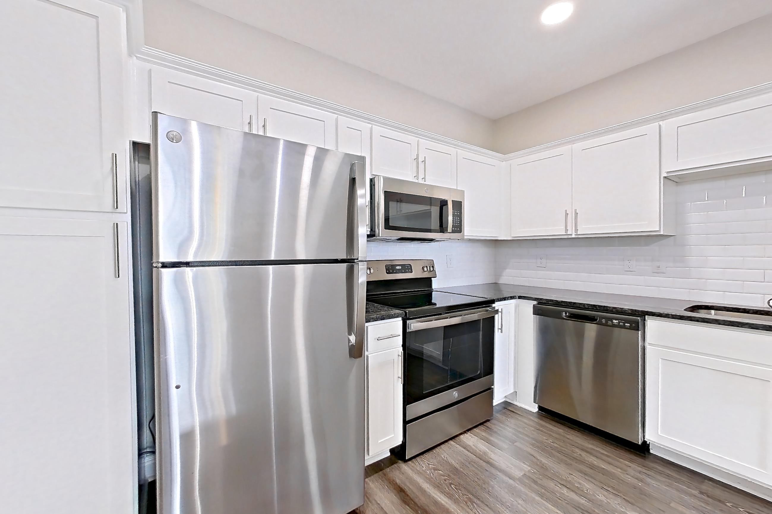 Kitchen with dark stone countertops, dark wood-finish flooring, dishwasher, electric range, light stone countertops, microwave, oven/range, refrigerator, and stainless steel appliances, Apartment 4508 at Marq Perimeter