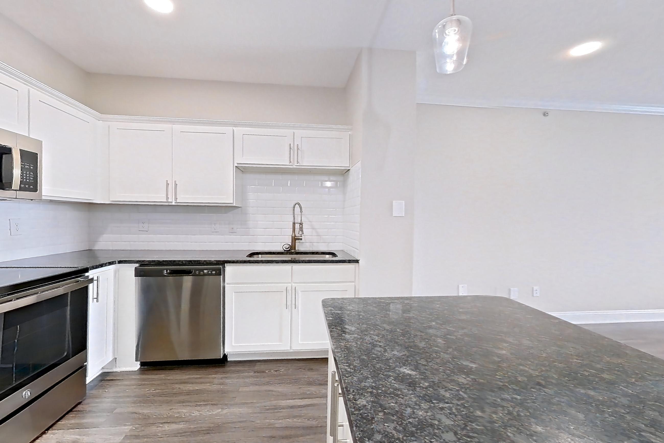 Kitchen with dark stone countertops, dark wood-finish flooring, dishwasher, electric range, light stone countertops, microwave, oven/range, refrigerator, and stainless steel appliances, Apartment 4508 at Marq Perimeter