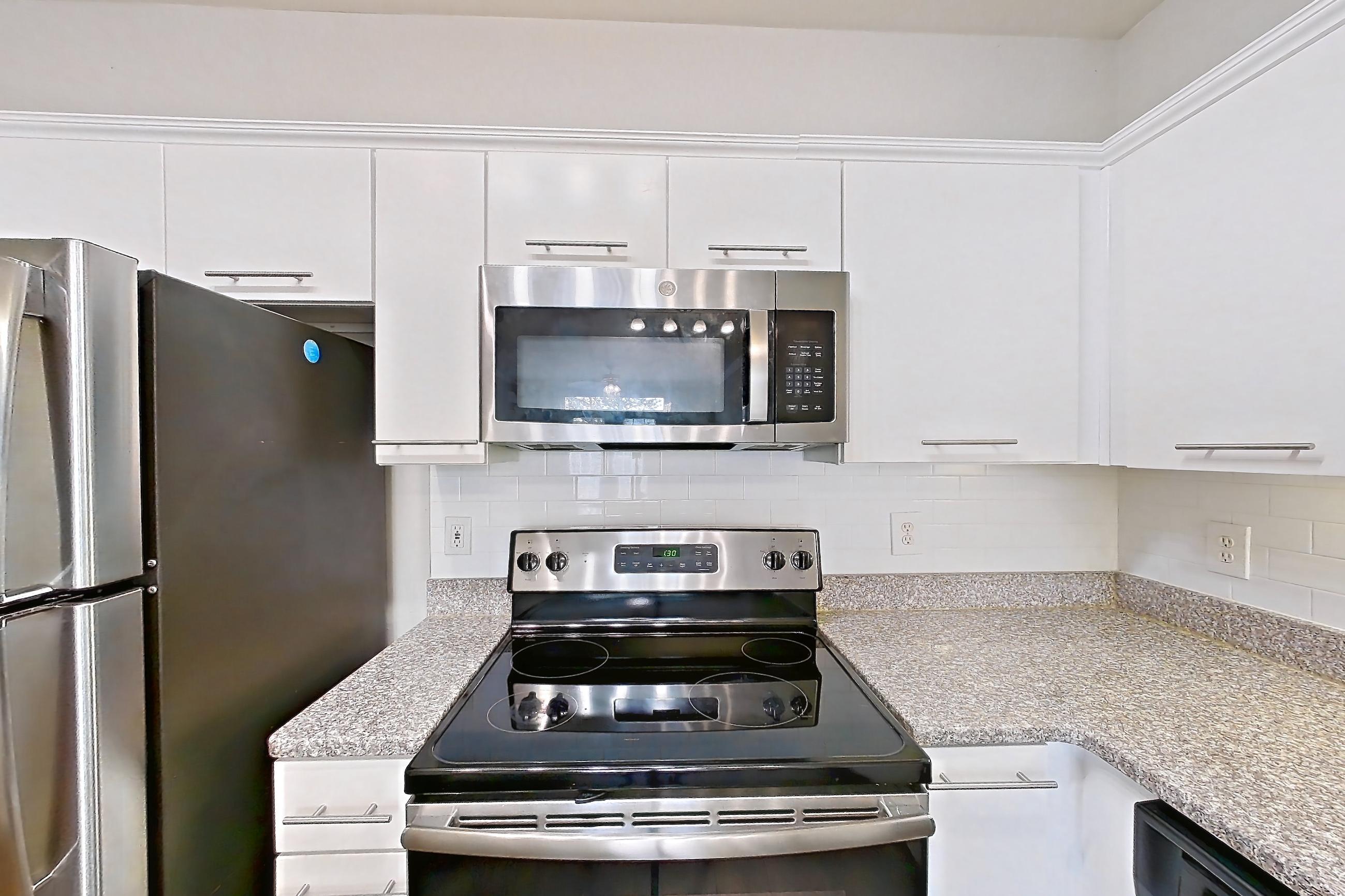 Kitchen with dark wood-finish flooring, dishwasher, electric range, light countertops, light stone countertops, microwave, oven/range, refrigerator, and stainless steel appliances, Apartment 4512 at Marq Perimeter