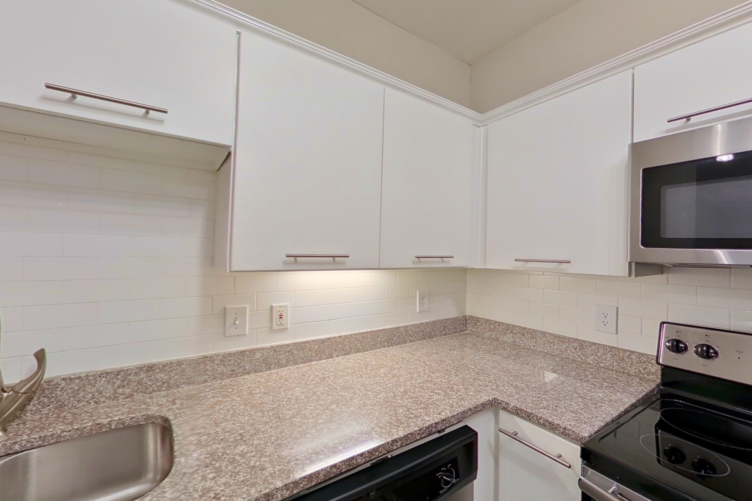 Kitchen with dishwasher, electric range, light countertops, light stone countertops, light wood-finish flooring, microwave, oven/range, refrigerator, and stainless steel appliances, Apartment 5104 at Marq Perimeter