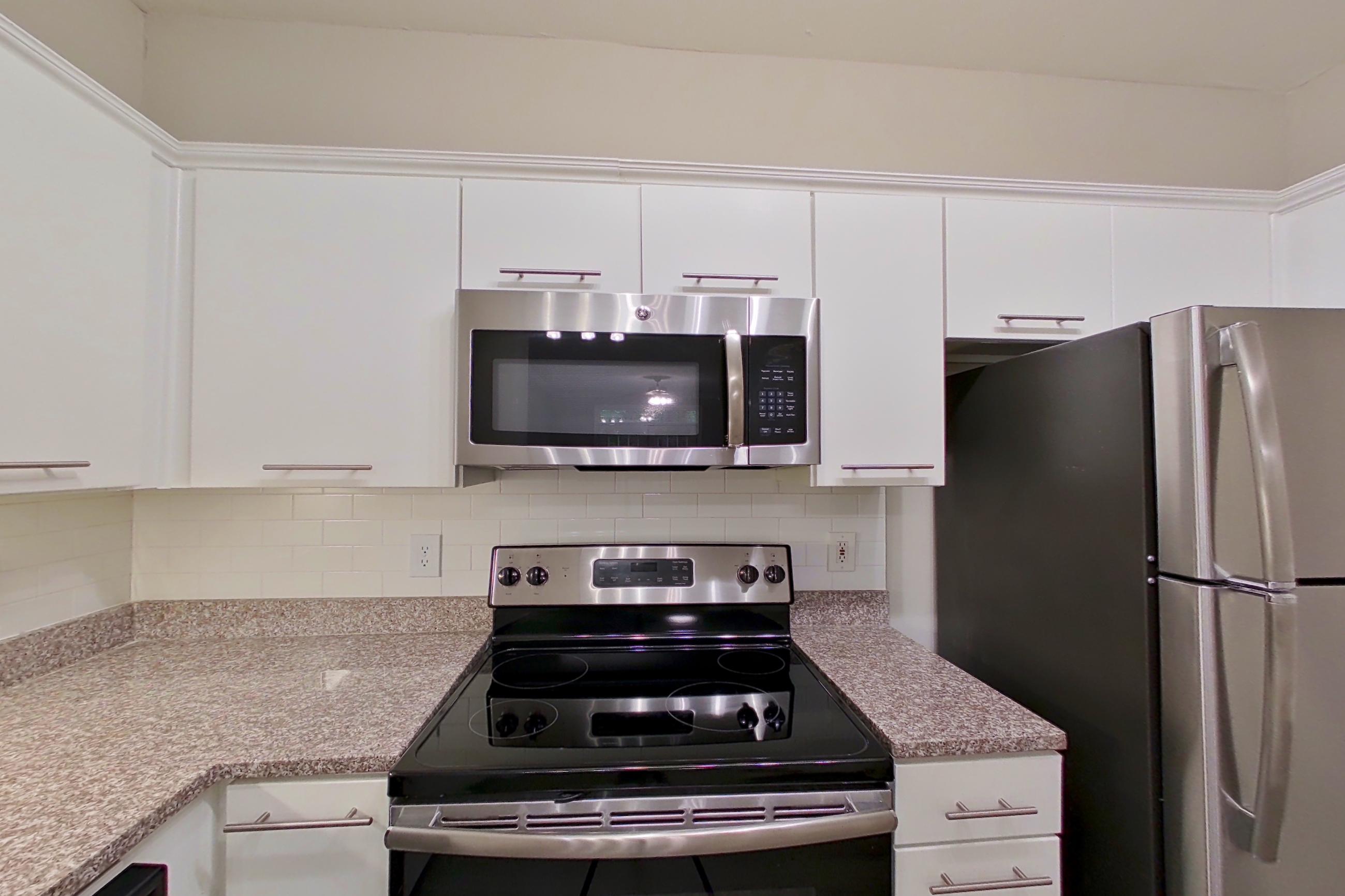 Kitchen with dishwasher, electric range, light countertops, light stone countertops, light wood-finish flooring, microwave, oven/range, refrigerator, and stainless steel appliances, Apartment 5104 at Marq Perimeter