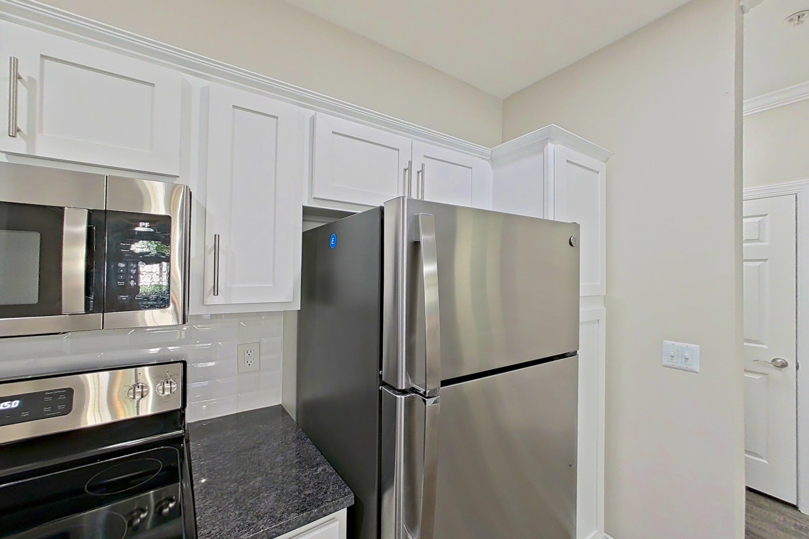 Kitchen with dark stone countertops, dishwasher, electric range, light countertops, light wood-finish flooring, microwave, oven/range, refrigerator, and stainless steel appliances, Apartment 5209 at Marq Perimeter