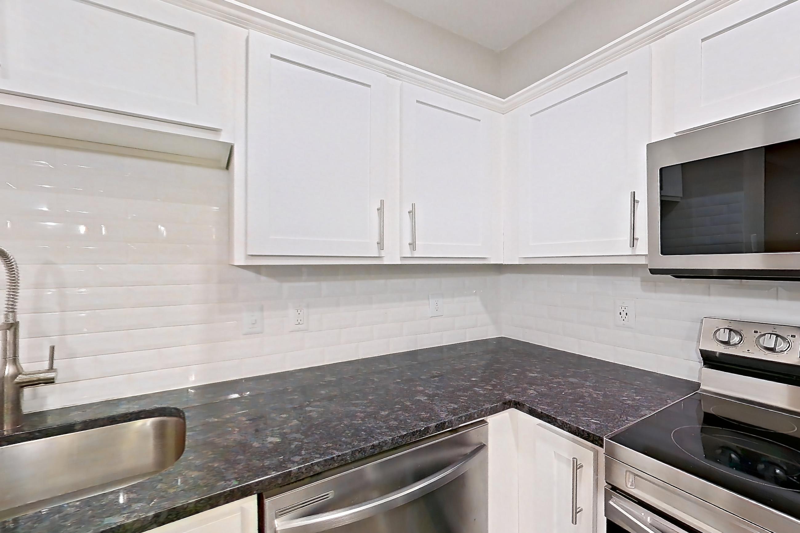 Kitchen with dark stone countertops, dishwasher, electric range, light stone countertops, light wood-finish flooring, microwave, oven/range, refrigerator, and stainless steel appliances, Apartment 5210 at Marq Perimeter