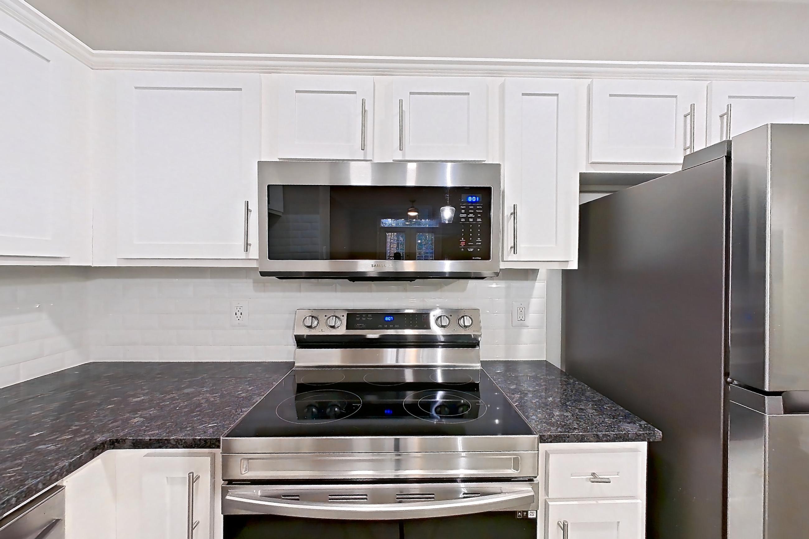 Kitchen with dark stone countertops, dishwasher, electric range, light stone countertops, light wood-finish flooring, microwave, oven/range, refrigerator, and stainless steel appliances, Apartment 5210 at Marq Perimeter