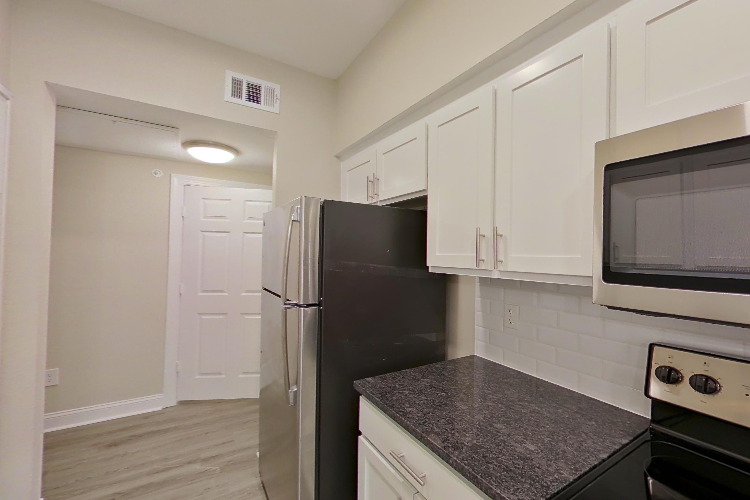 Kitchen with dark stone countertops, dishwasher, electric range, light countertops, light wood-finish flooring, microwave, oven/range, refrigerator, and stainless steel appliances, Apartment 5213 at Marq Perimeter