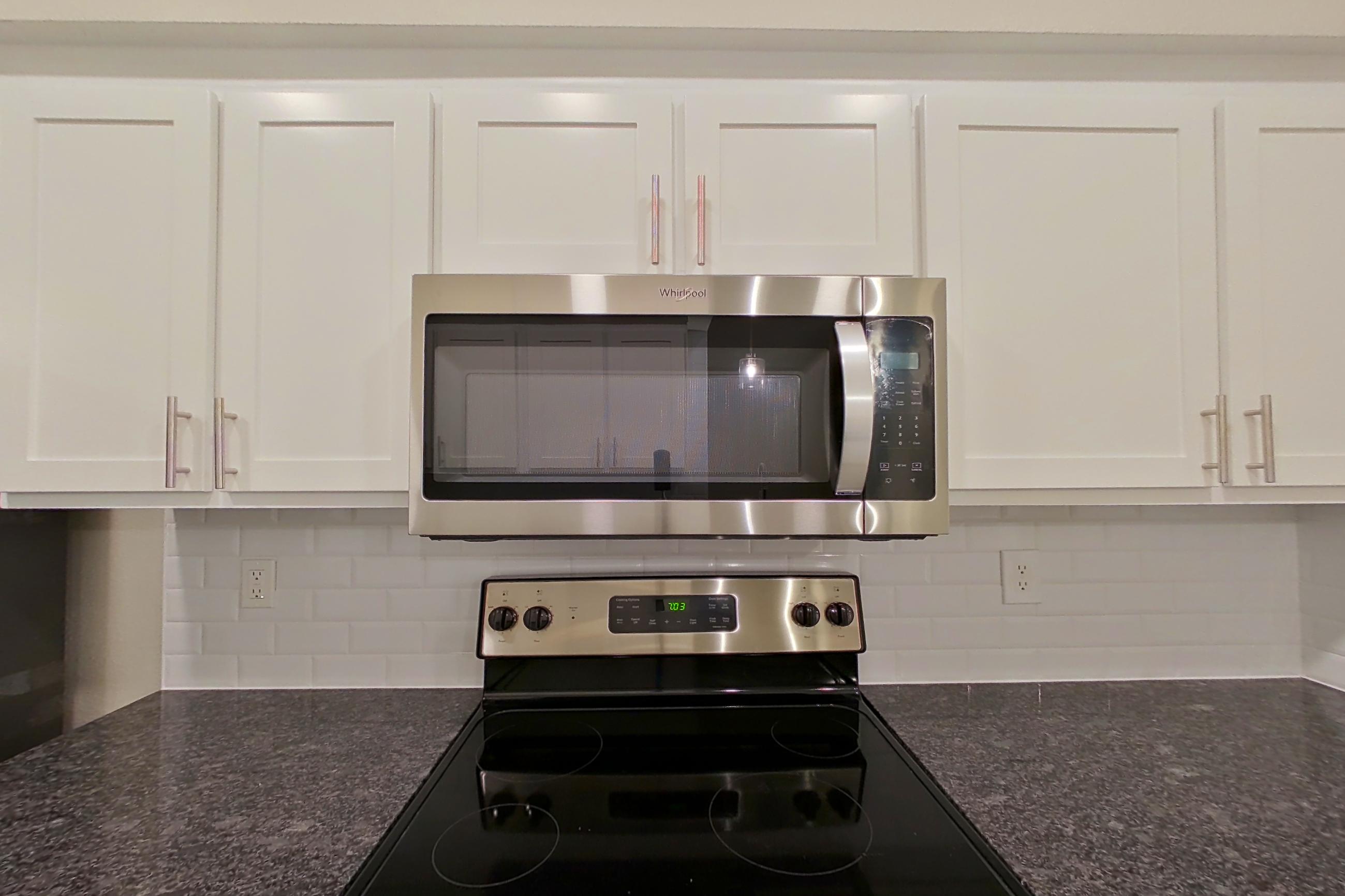Kitchen with dark stone countertops, dishwasher, electric range, light countertops, light wood-finish flooring, microwave, oven/range, refrigerator, and stainless steel appliances, Apartment 5213 at Marq Perimeter