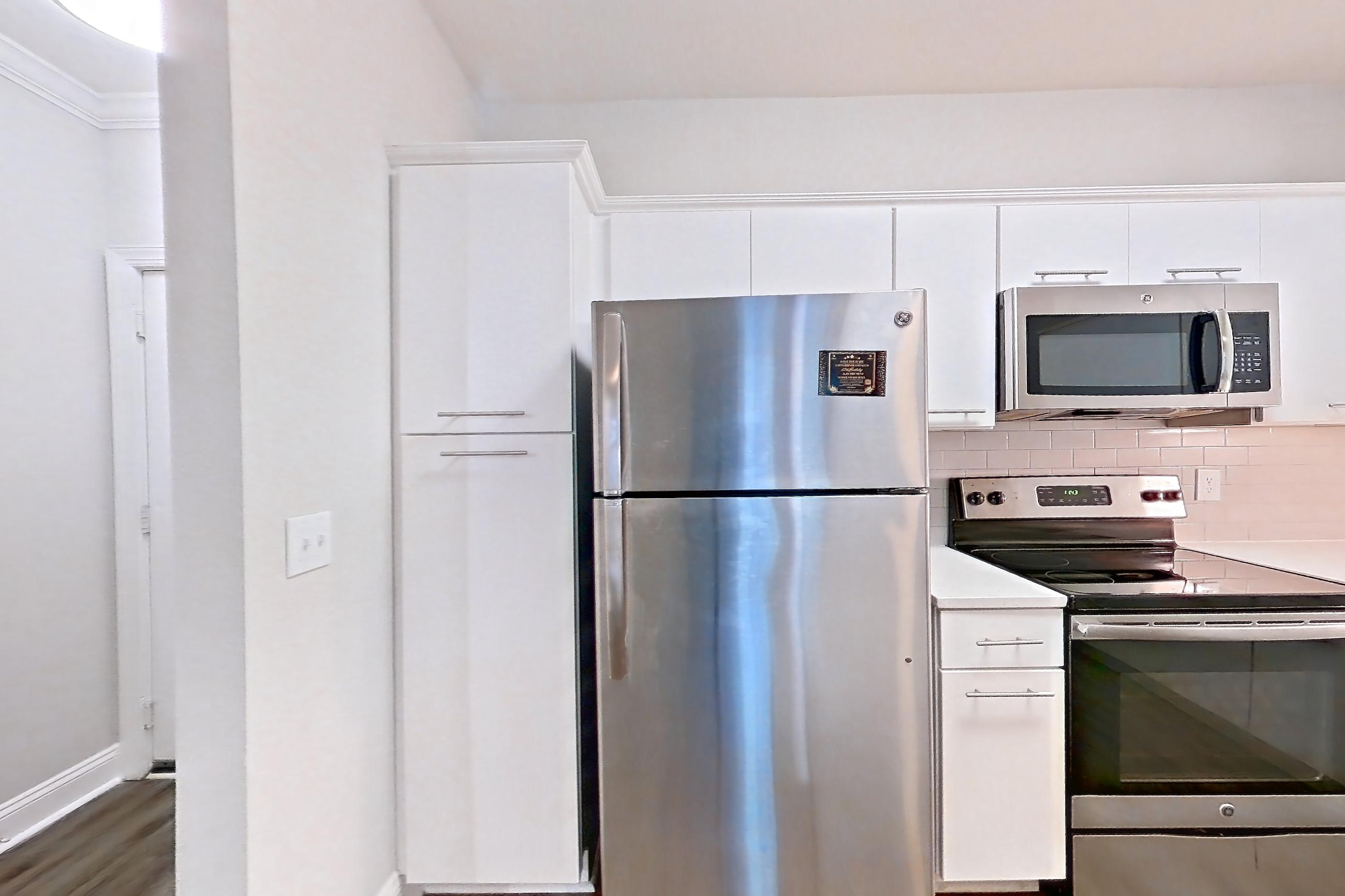 Kitchen with dark wood-finish flooring, electric range, kitchen island, light countertops, light stone countertops, light wood-finish flooring, microwave, oven/range, refrigerator, and stainless steel appliances, Apartment 5303 at Marq Perimeter