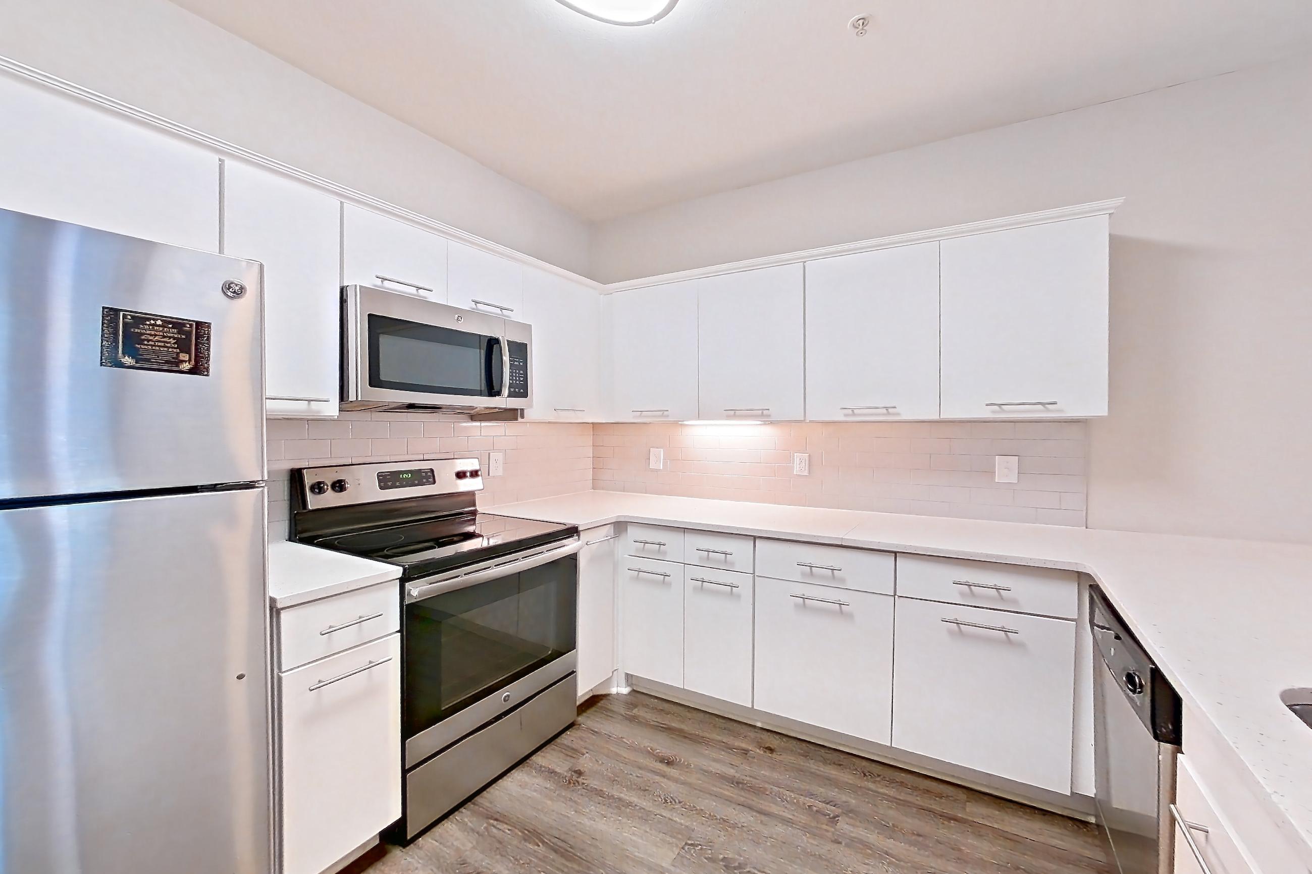Kitchen with dark wood-finish flooring, electric range, kitchen island, light countertops, light stone countertops, light wood-finish flooring, microwave, oven/range, refrigerator, and stainless steel appliances, Apartment 5303 at Marq Perimeter