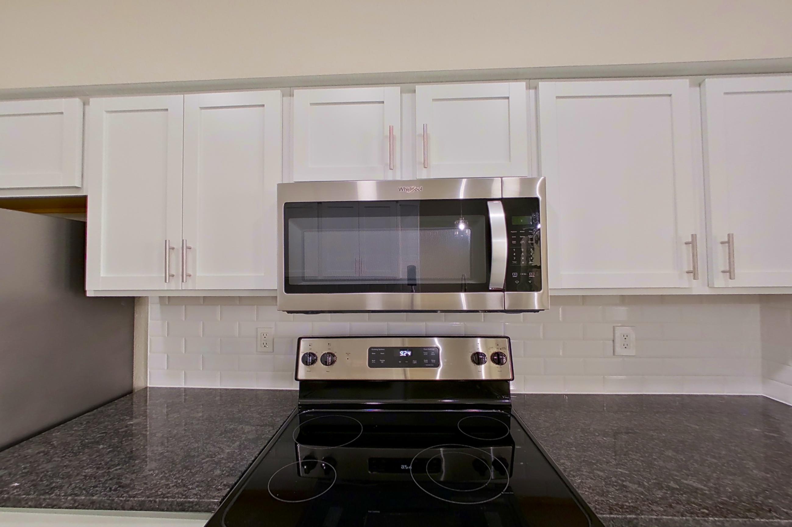 Kitchen with dark stone countertops, dishwasher, electric range, light countertops, light wood-finish flooring, microwave, oven/range, refrigerator, and stainless steel appliances, Apartment 5313 at Marq Perimeter