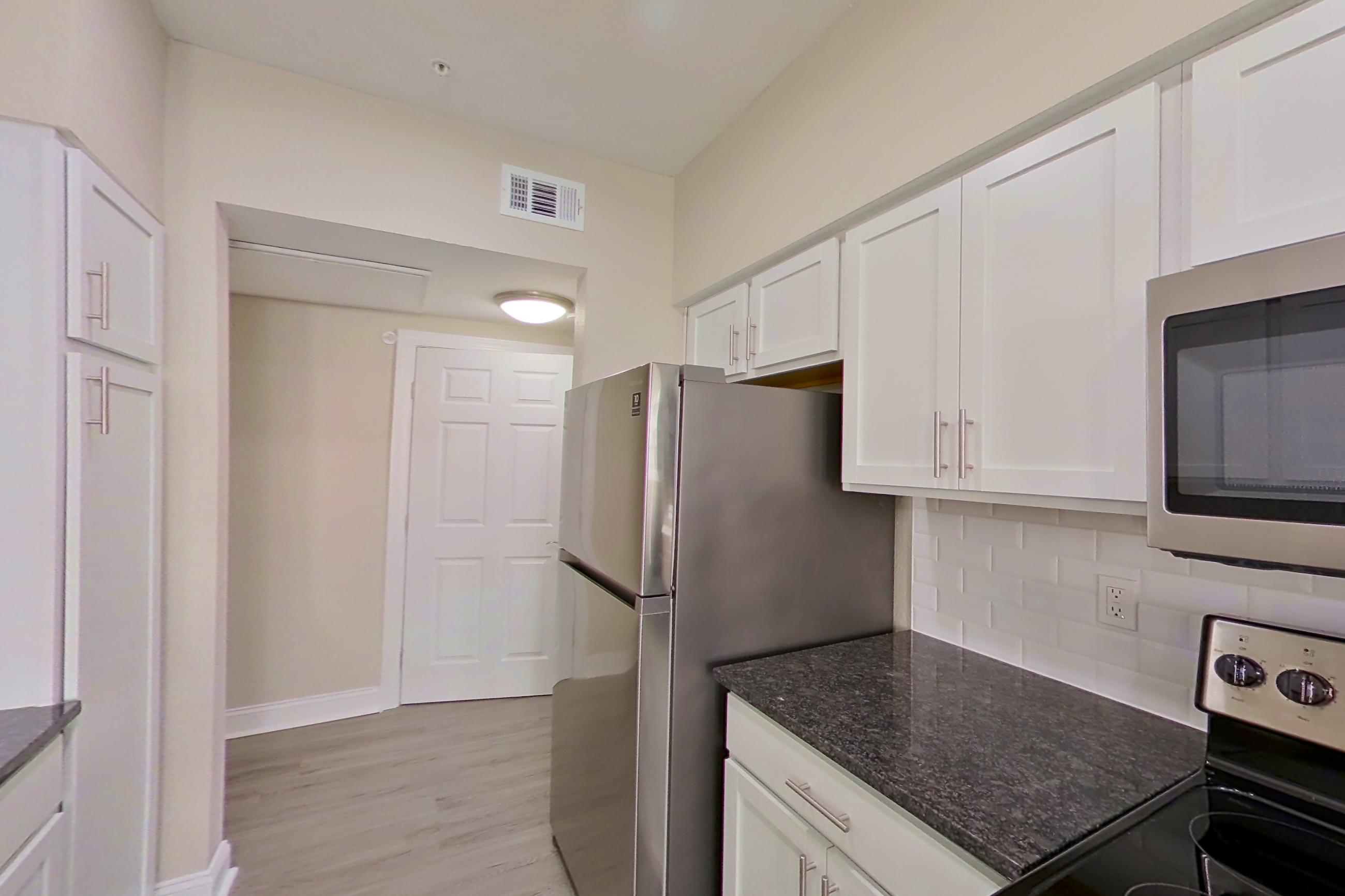 Kitchen with dark stone countertops, dishwasher, electric range, light countertops, light wood-finish flooring, microwave, oven/range, refrigerator, and stainless steel appliances, Apartment 5313 at Marq Perimeter