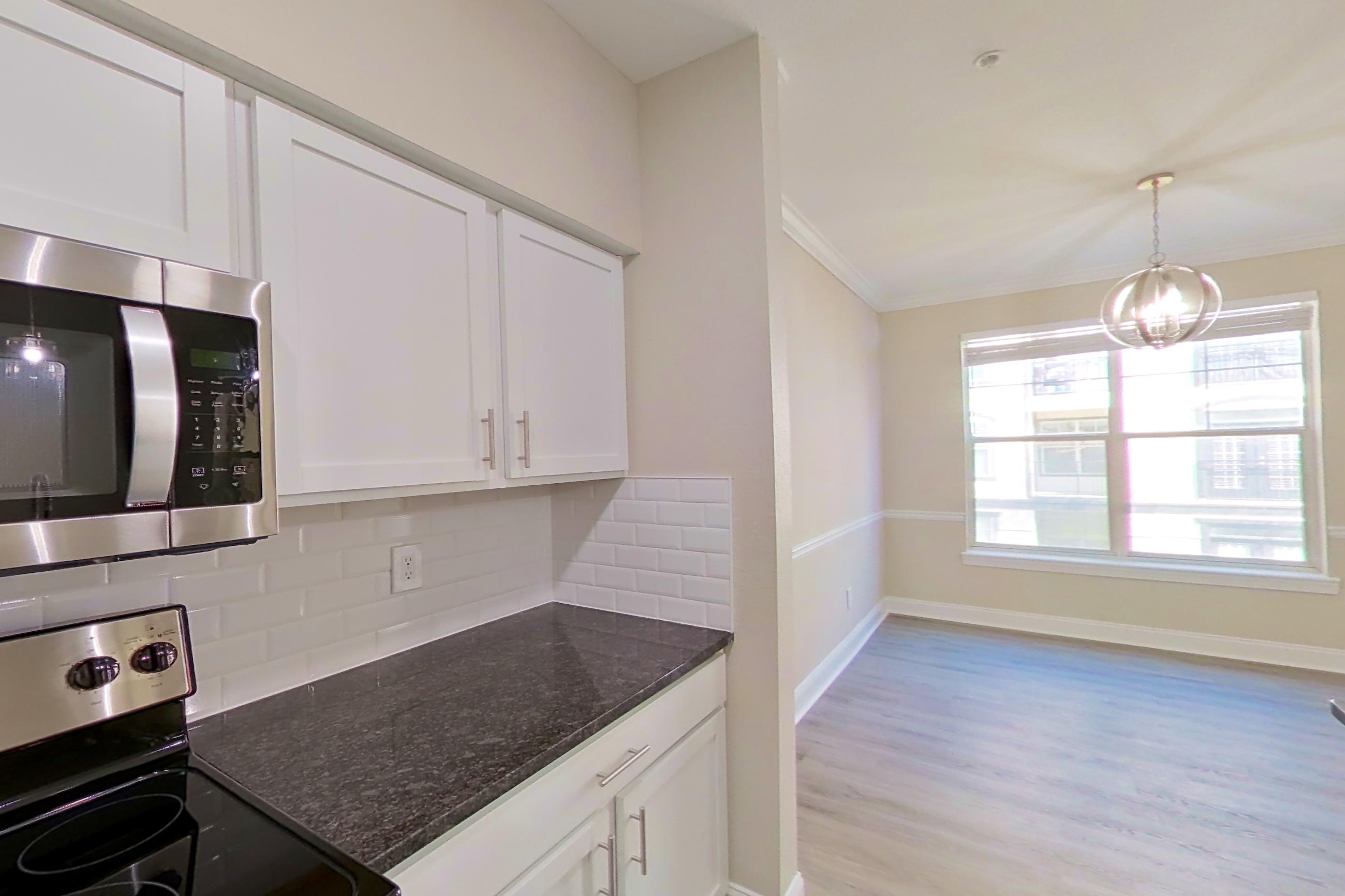 Kitchen with dark stone countertops, dishwasher, electric range, light countertops, light wood-finish flooring, microwave, oven/range, refrigerator, and stainless steel appliances, Apartment 5313 at Marq Perimeter